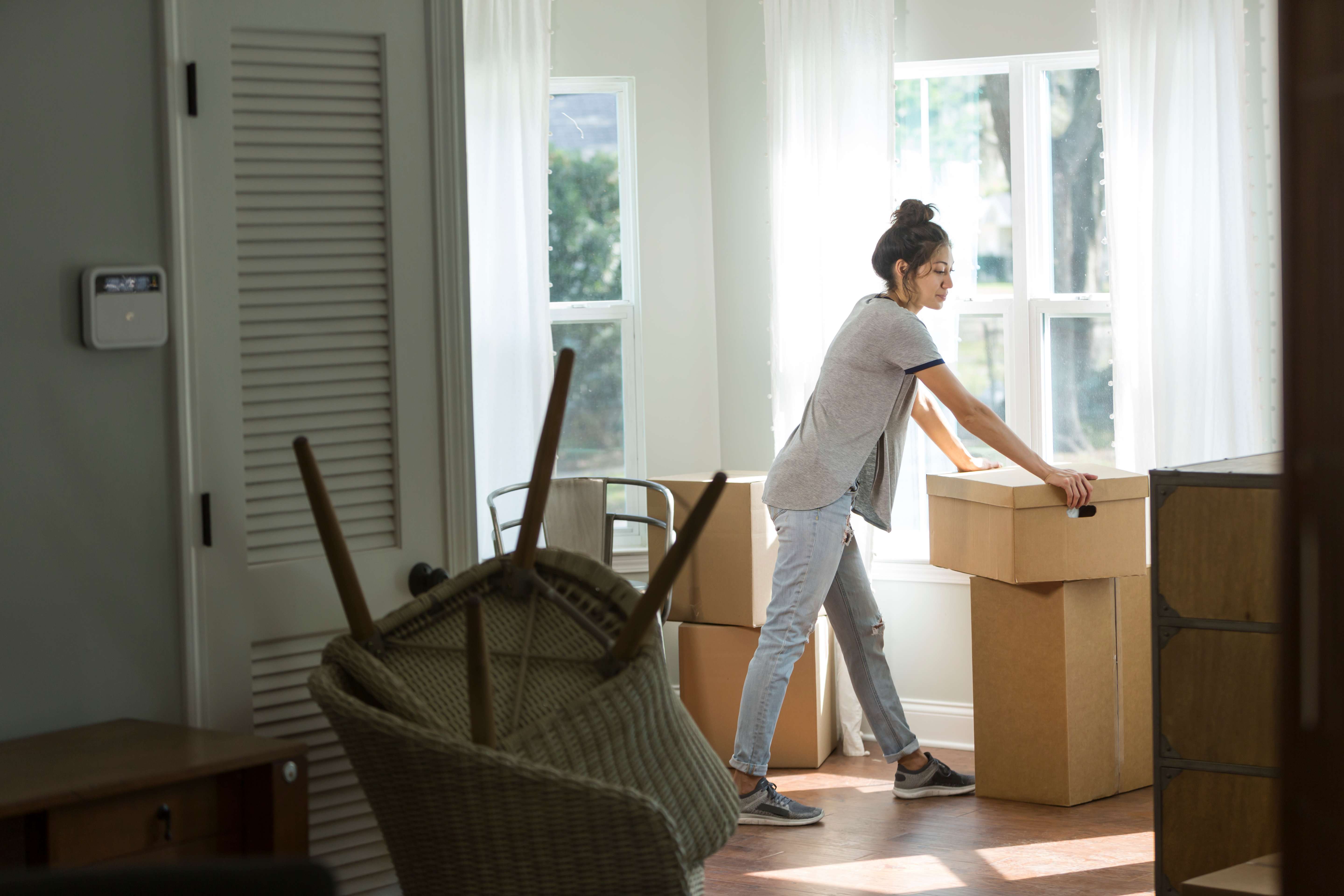 Woman moving cardboard boxes inside a sunlit room during a home move