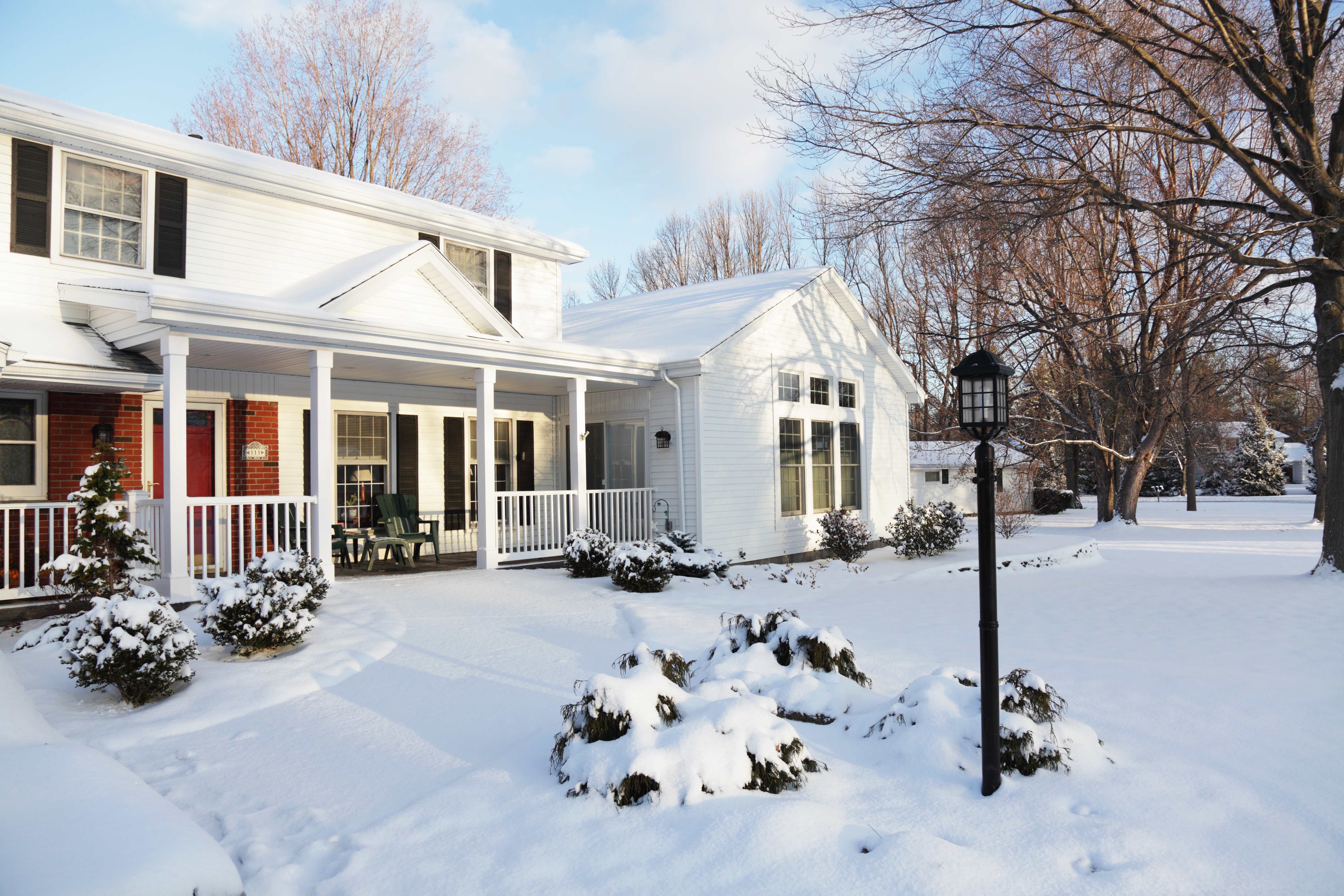 White suburban house with front porch and snow-covered yard in winter