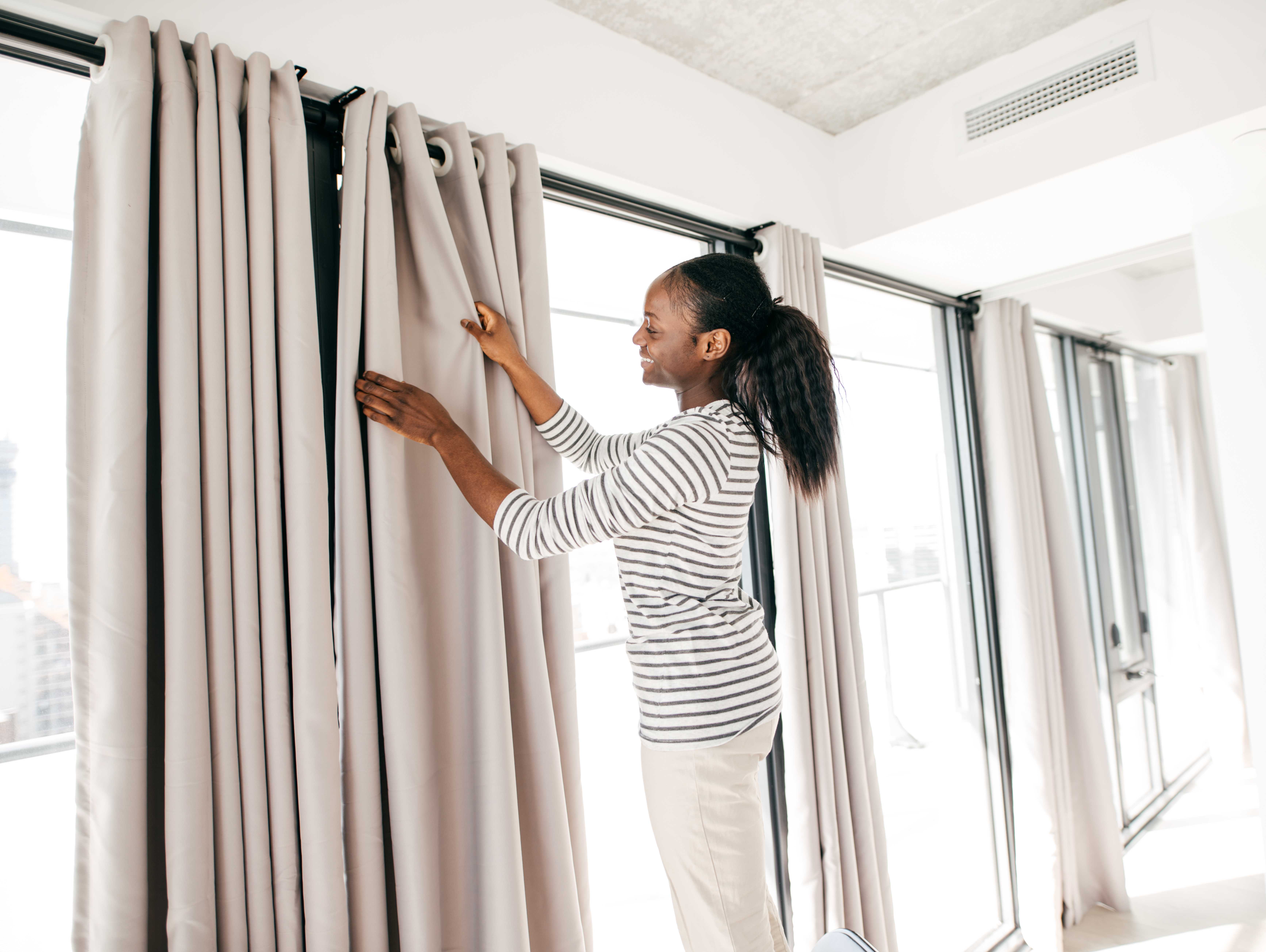 Woman closes heavy drapes in winter to increase energy-efficiency in the cold