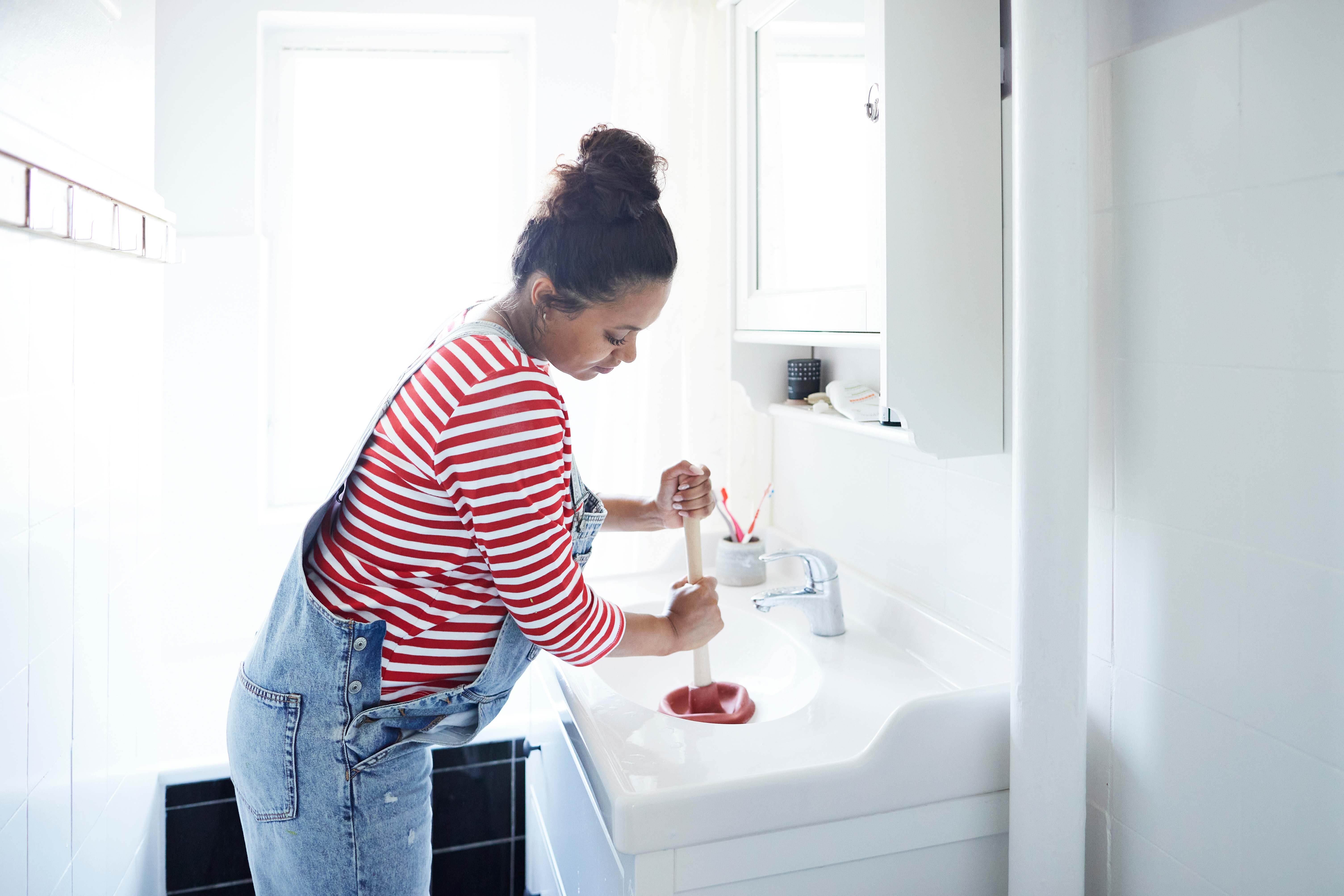 Woman using a plunger to unclog a bathroom sink