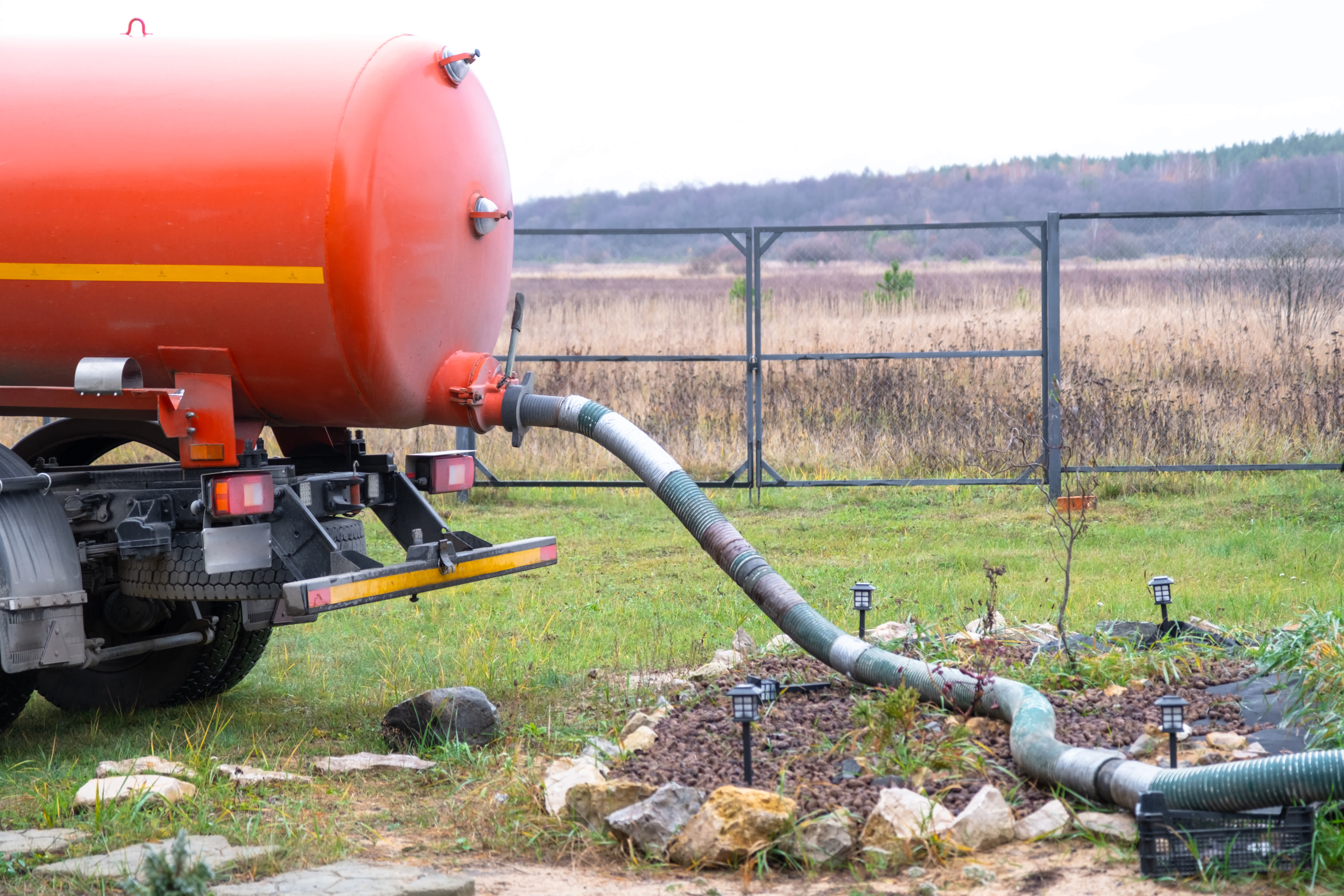 Orange septic tank truck with a large hose connected to the ground for waste pumping