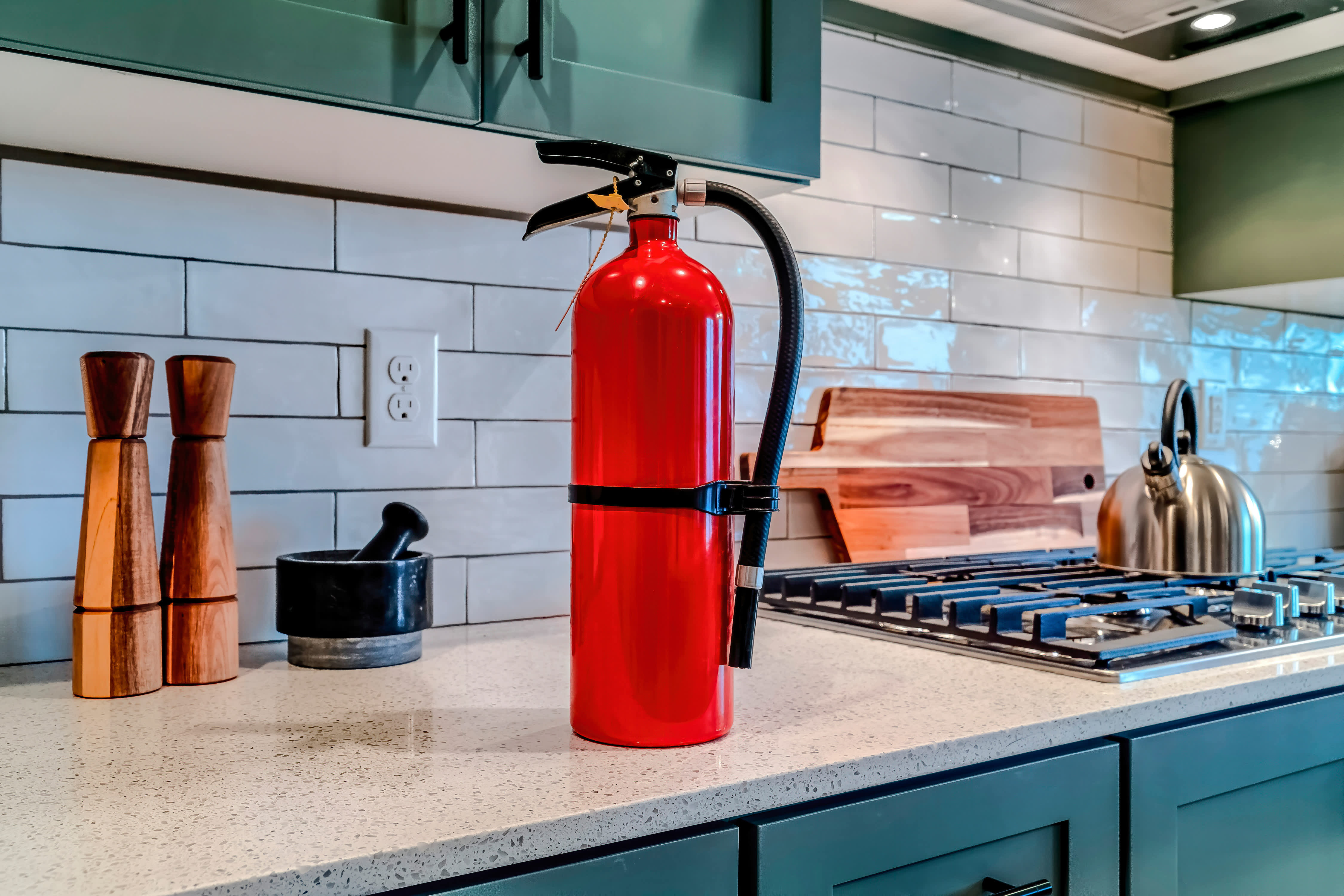 Red fire extinguisher placed beside a cooktop on a kitchen countertop, highlighting home safety and preparedness