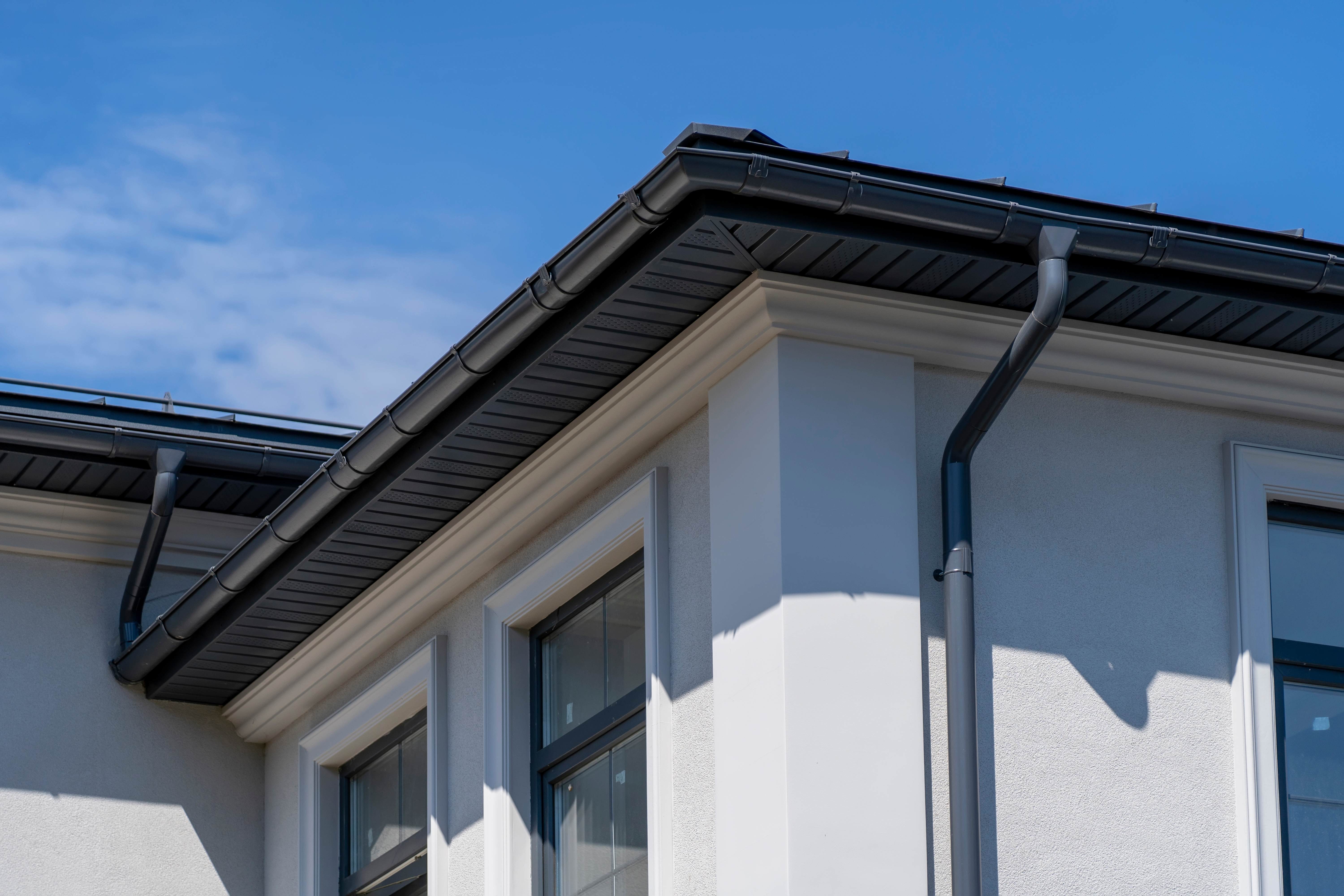Close-up view of house gutters and downspouts installed along the roofline against a clear blue sky.