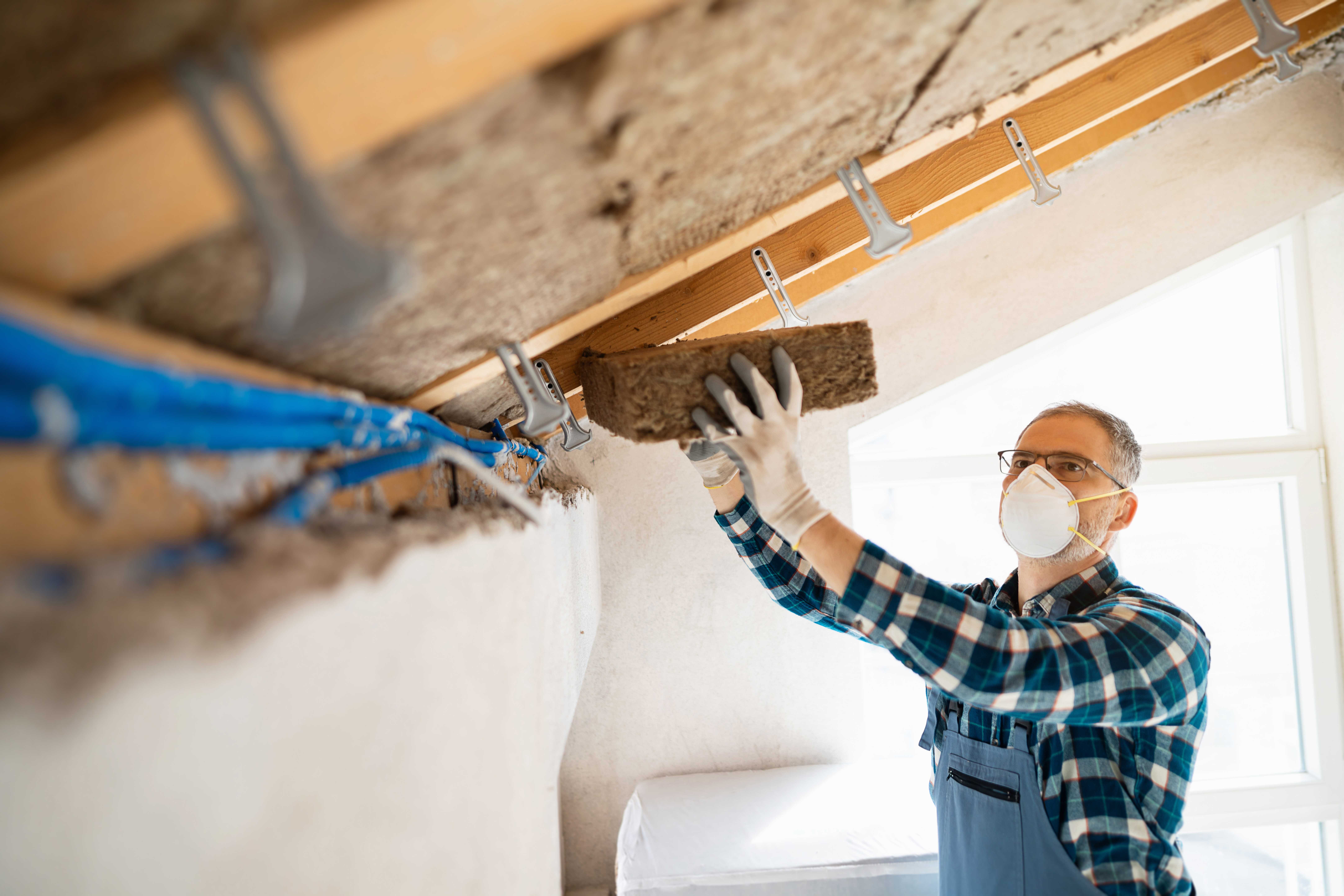 Worker installing mineral wool insulation in a ceiling