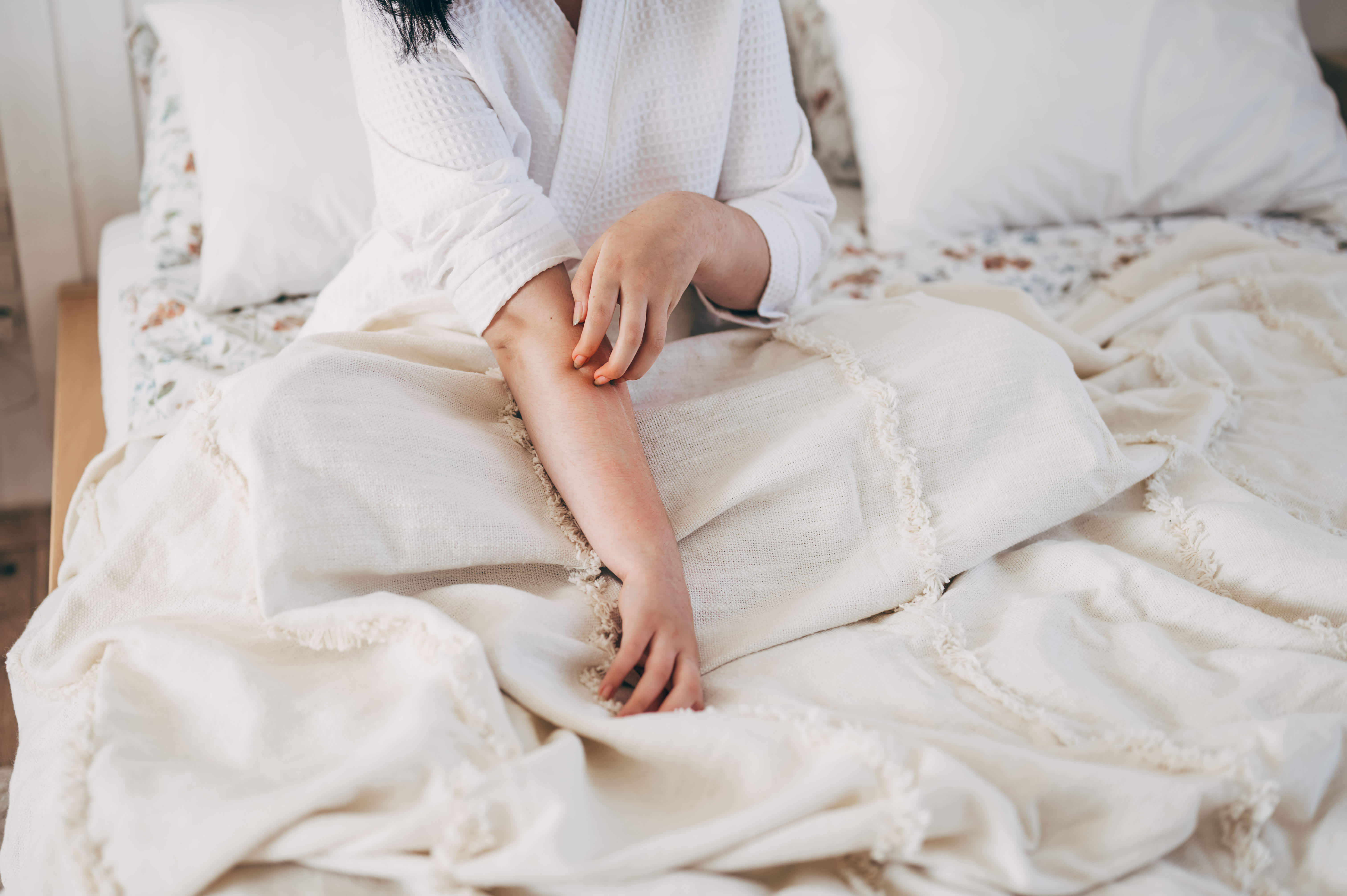 A person in bed scratching their arm due to a skin irritation