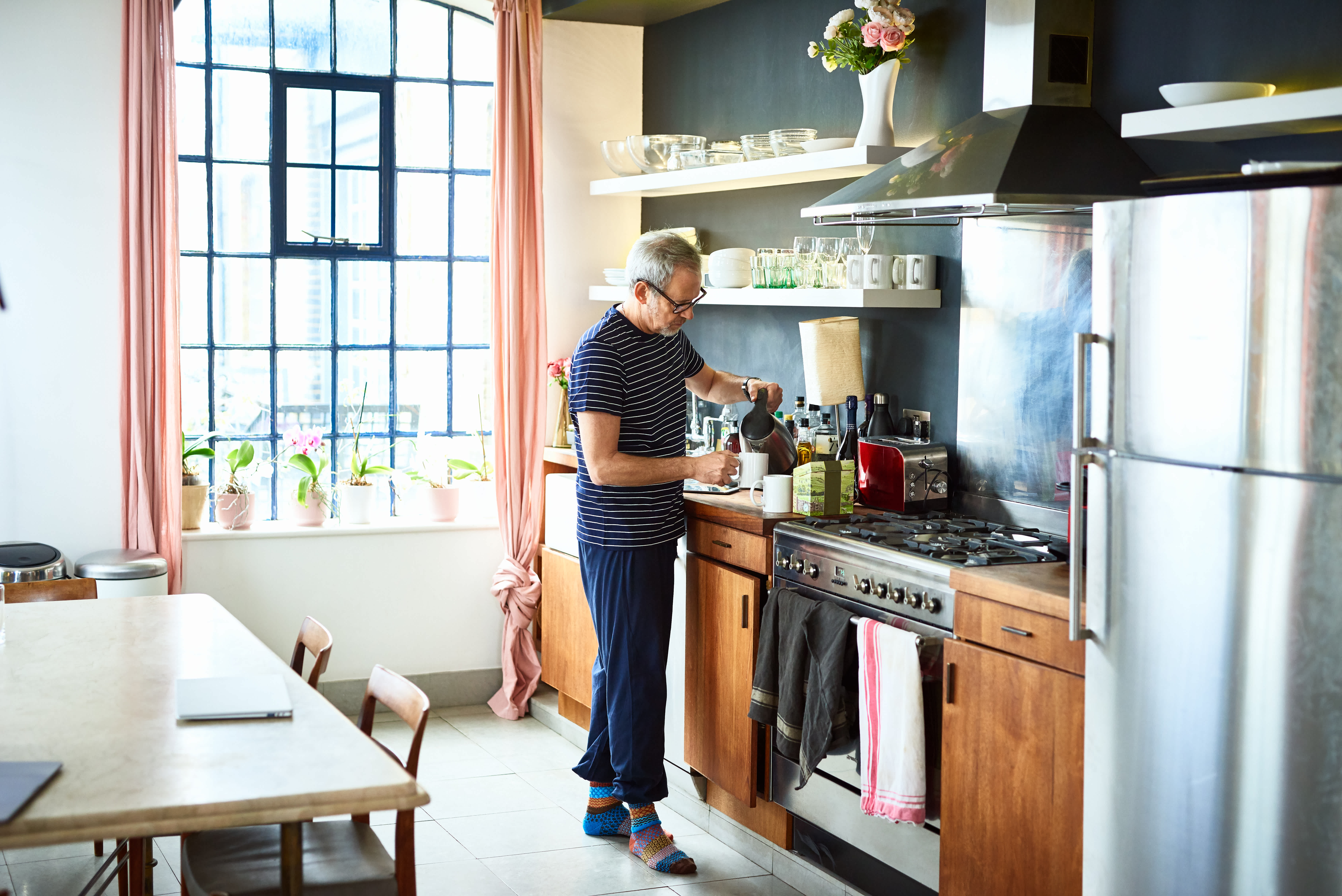 Mature man in the kitchen pouring hot water into a cup