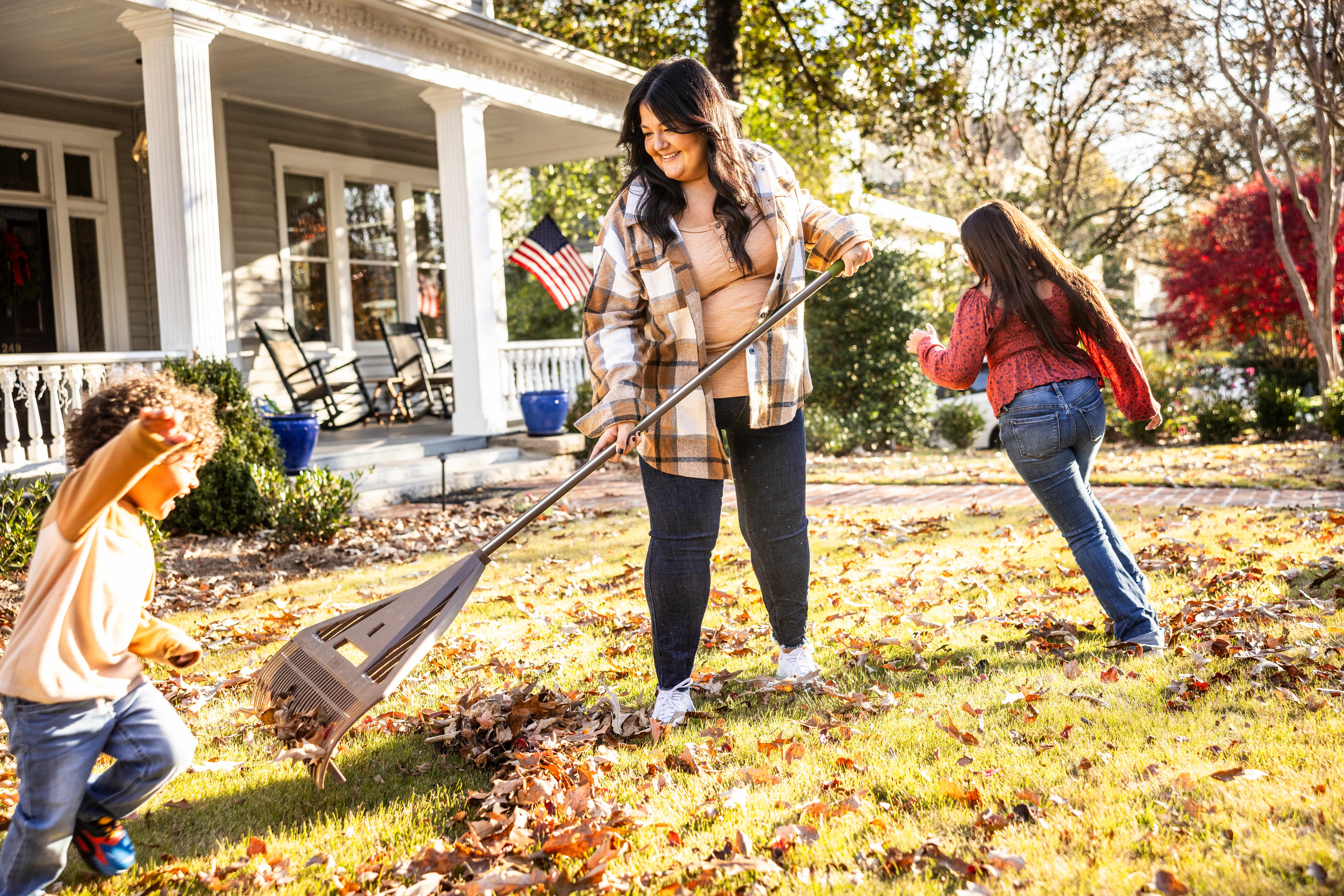 Mother raking leaves in front yard with kids