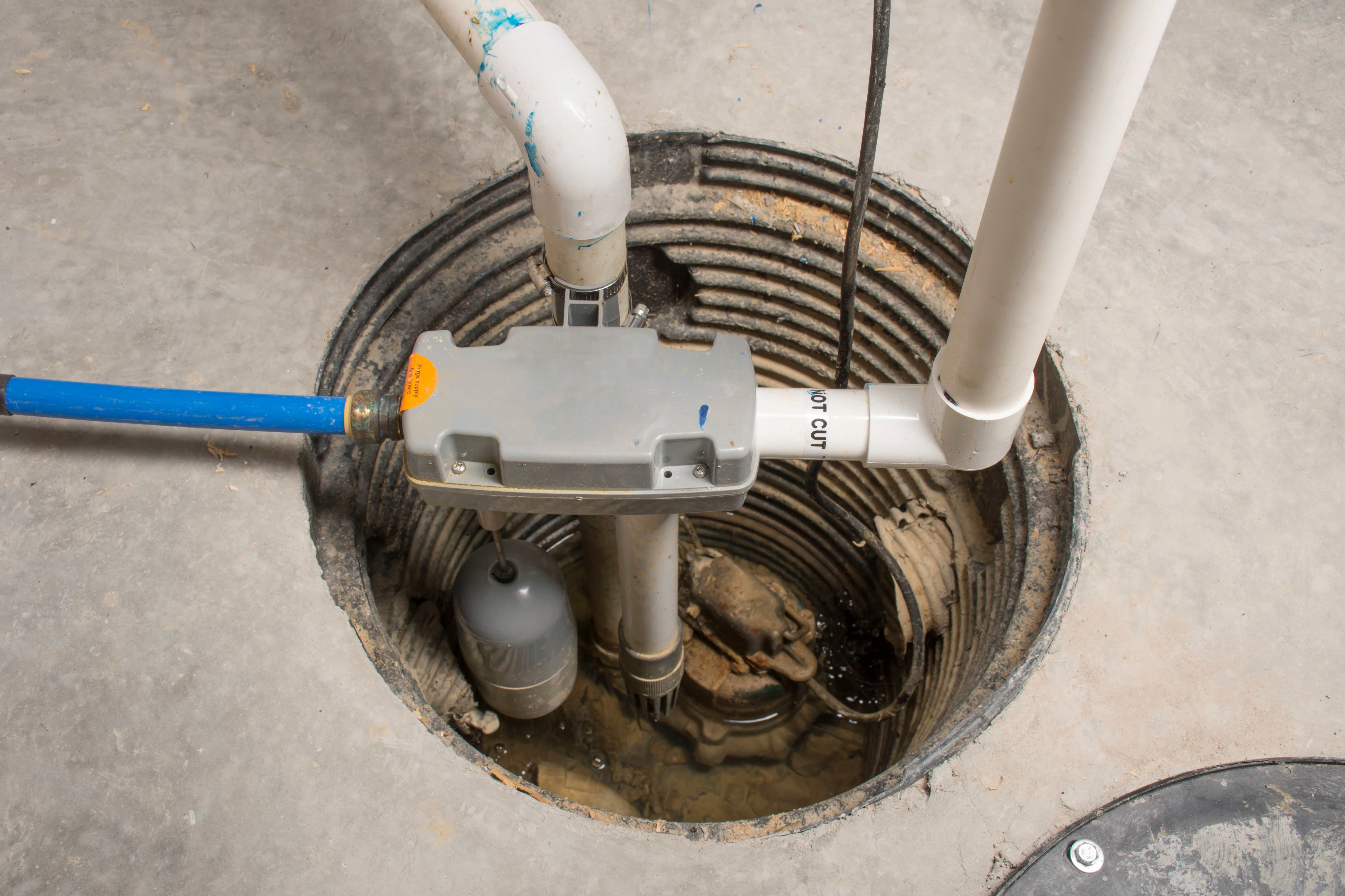 Installed sump pump system with connected PVC pipes and discharge line inside a basement pit