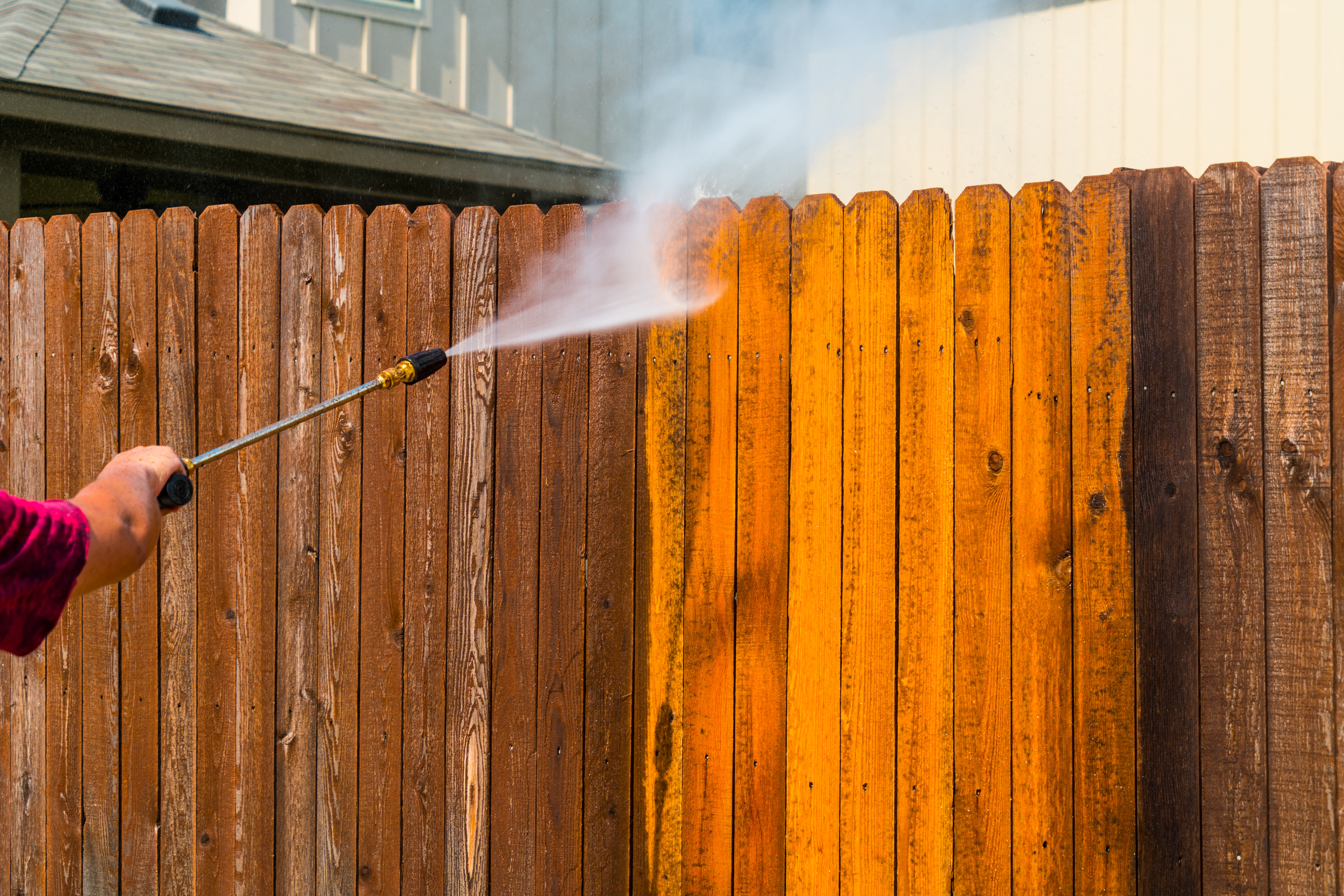 Person using a power washer to clean a wooden fence