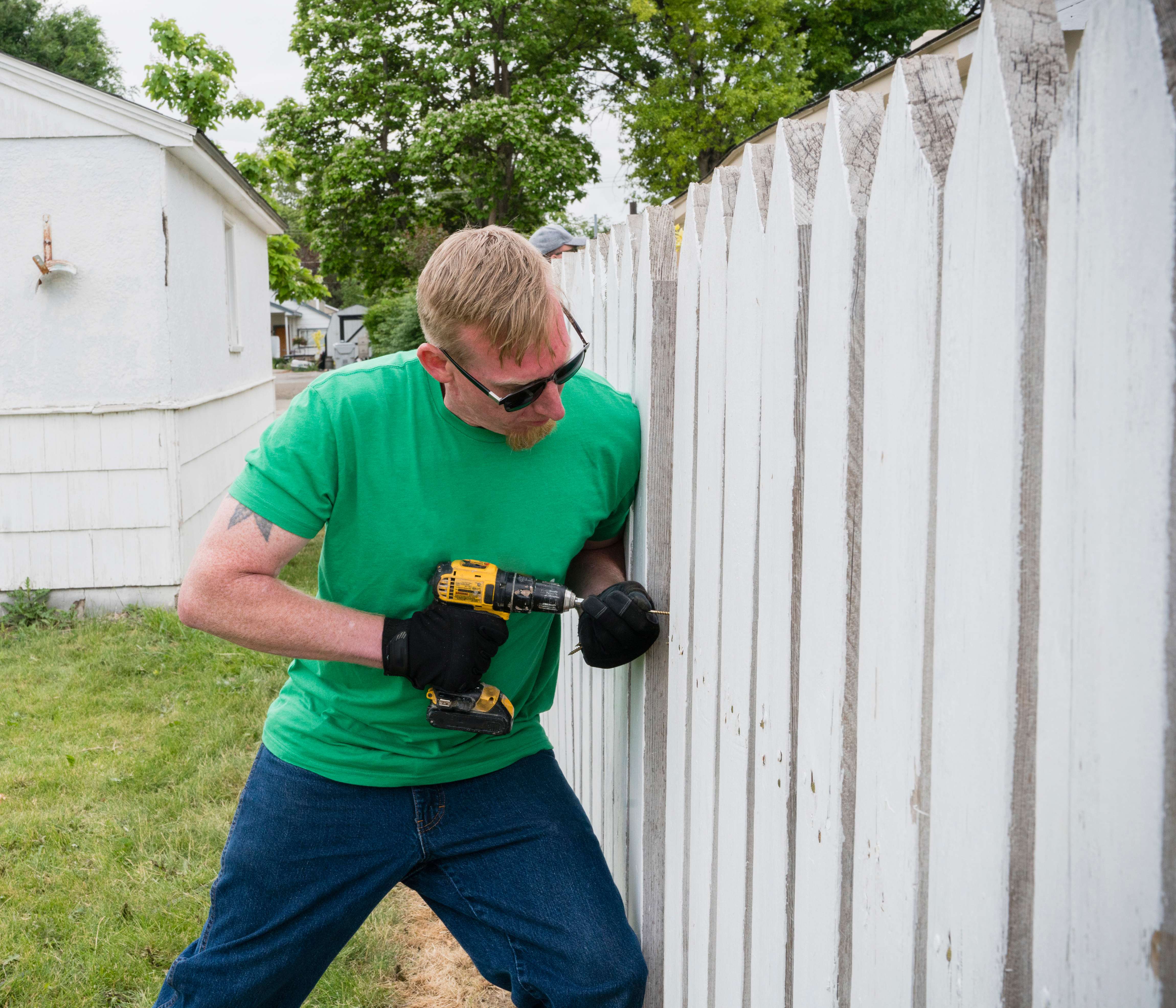 Handy person using a drill to repair a wooden fence