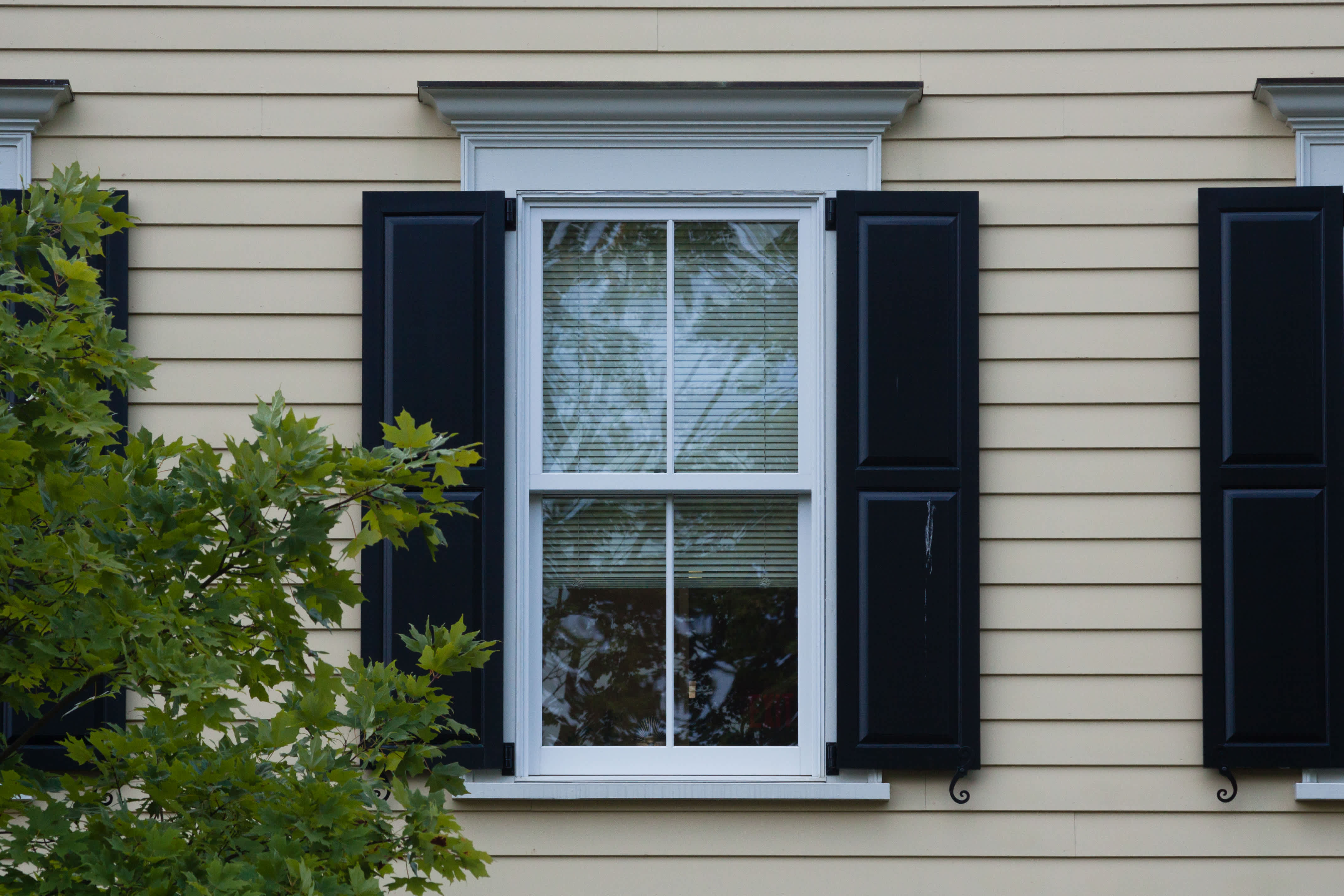 Exterior view of a double-hung window with black shutters on a beige house siding