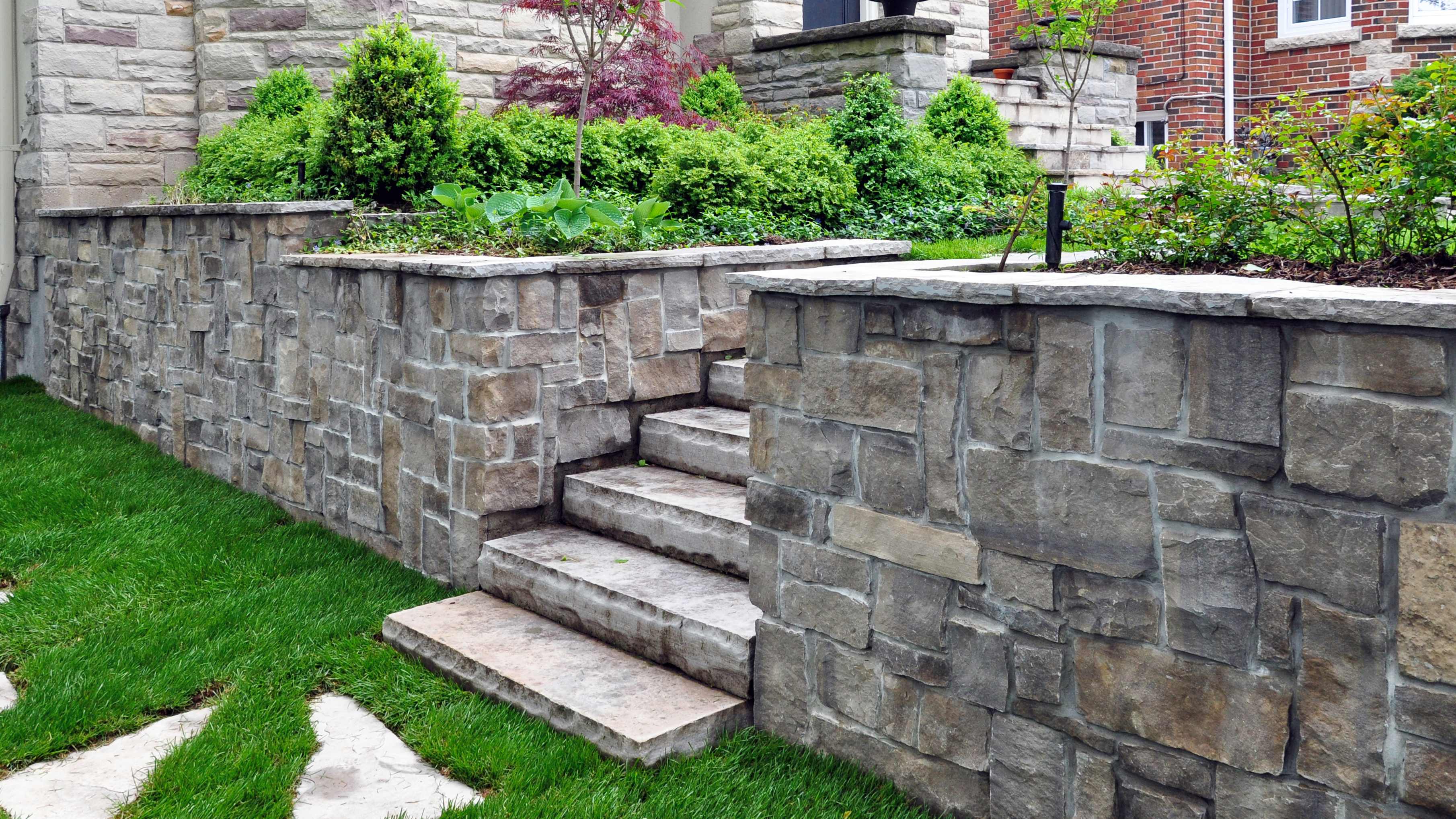 Stone retaining wall with built-in steps leading up to a landscaped garden with lush greenery and shrubs