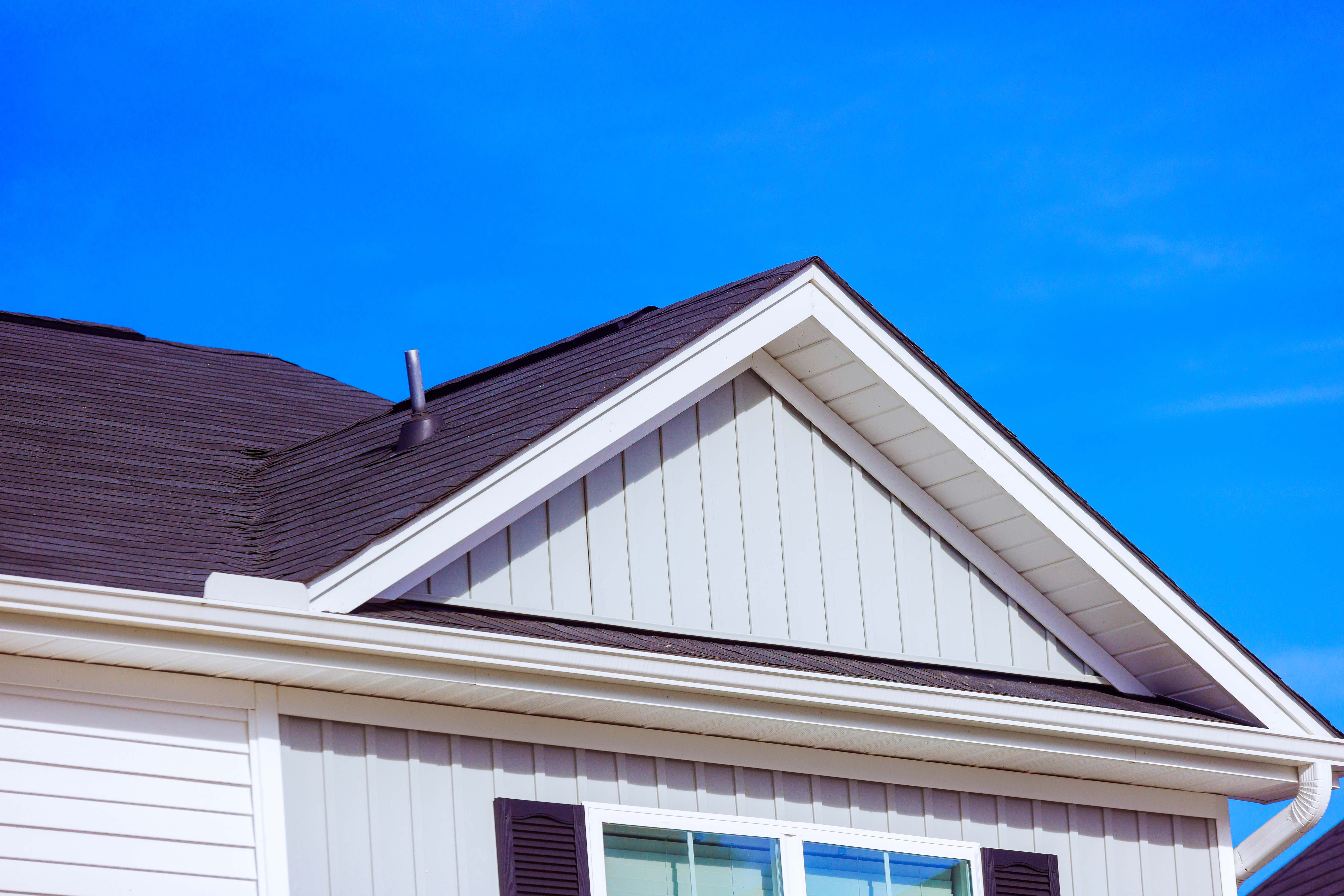 House with newly installed soffit, fascia, and board and batten siding against a blue sky.