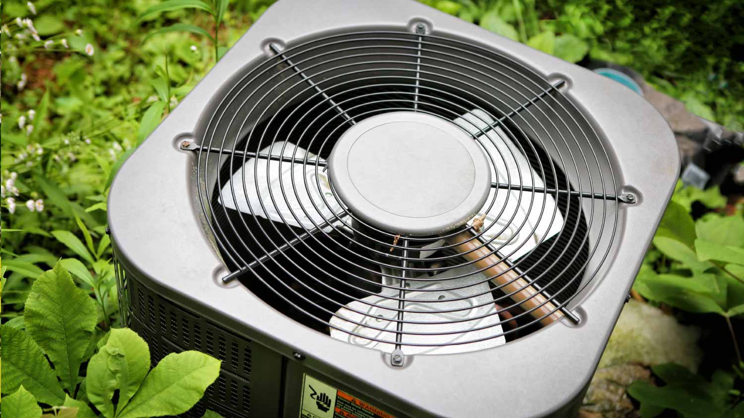 Air conditioner in grown greenery on background