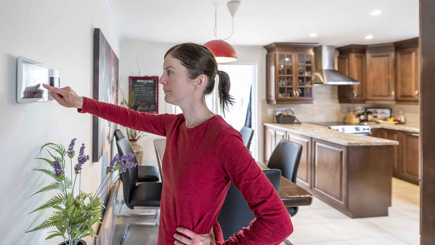 Woman using smart thermostat to adjust the temperature in the house