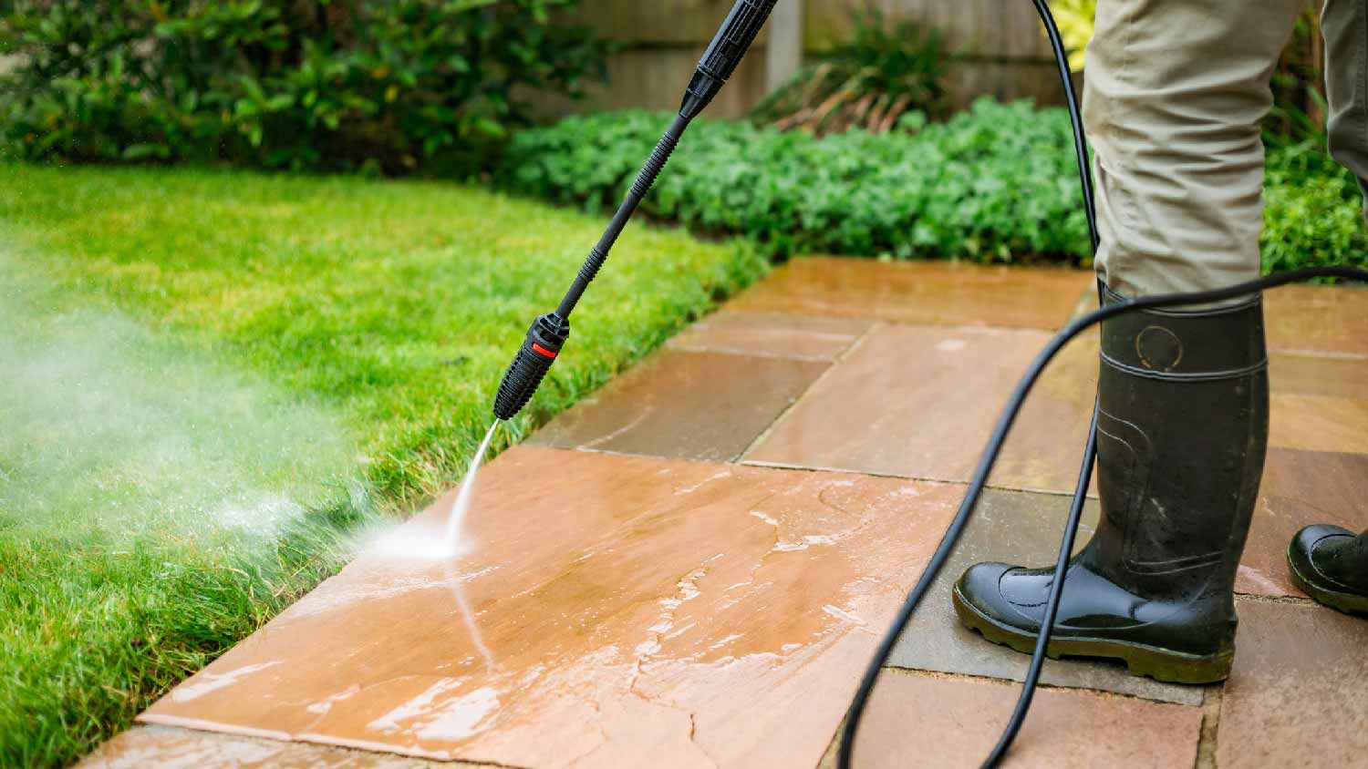 Senior man using a pressure washer to clean patio tiles outdoors