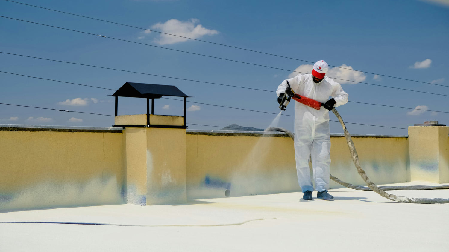 a man in overalls spraying foam on flat roof