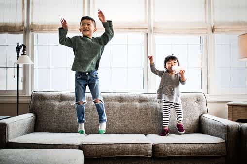 Siblings jumping on a couch at home