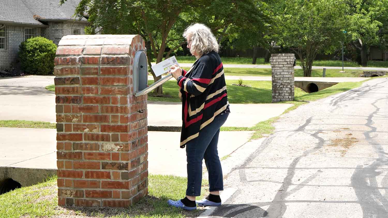 Woman checking a brick mailbox in a residential area