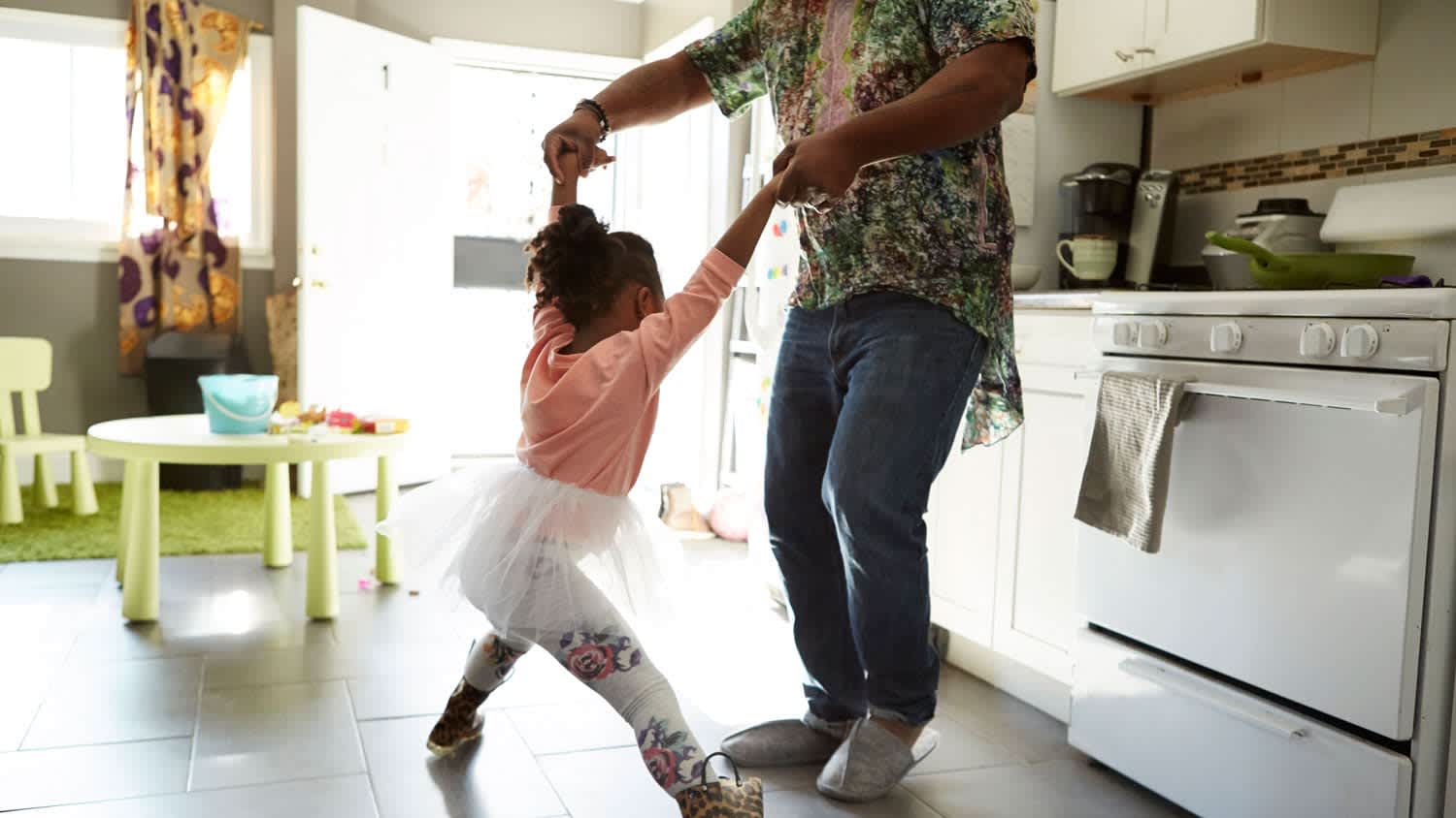 A father and his daughter dancing in a floor tiled kitchen