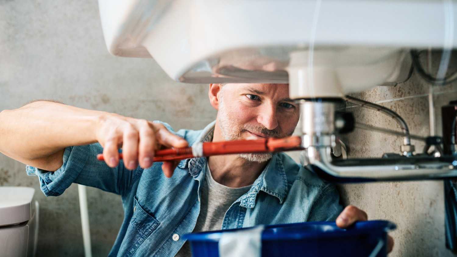 Man trying to fix a leak in a sink using a pipe wrench