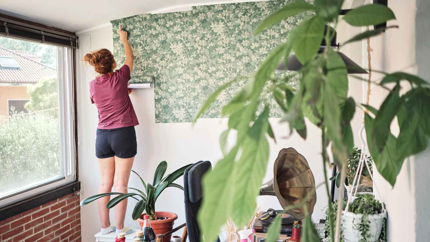Alt Text: Woman hanging vinyl wallpaper in the room