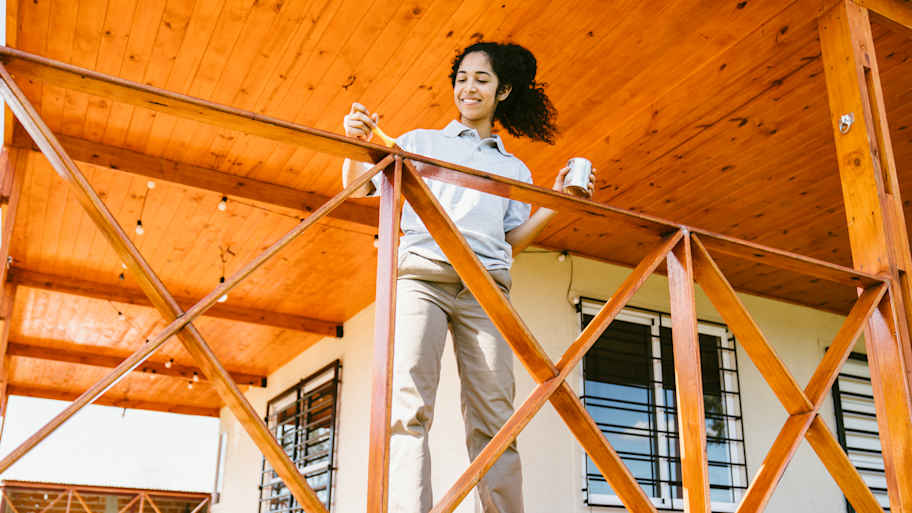 Smiling woman painting a wooden deck railing