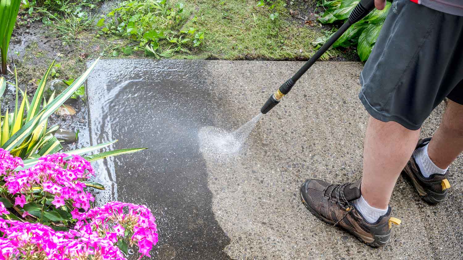 Person using a pressure washer to clean a concrete patio