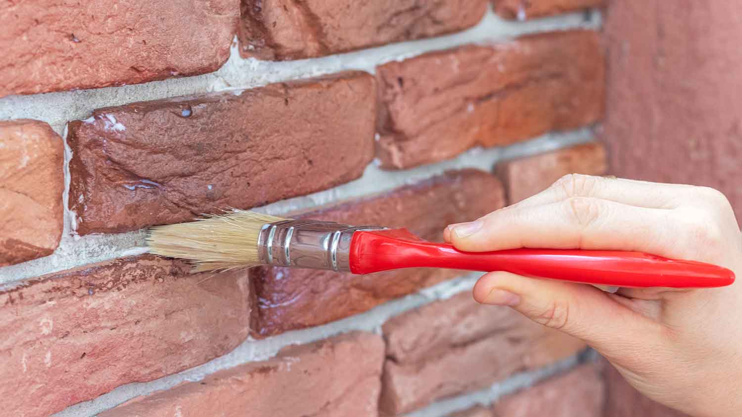 Woman using a brush to apply sealant on a brick wall