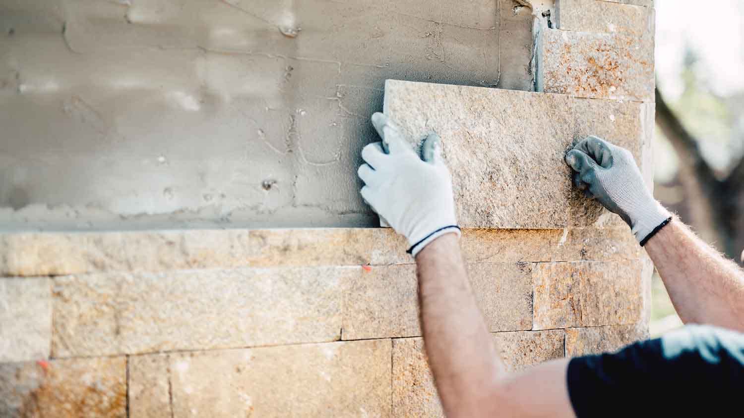 Worker installing stone siding on the house