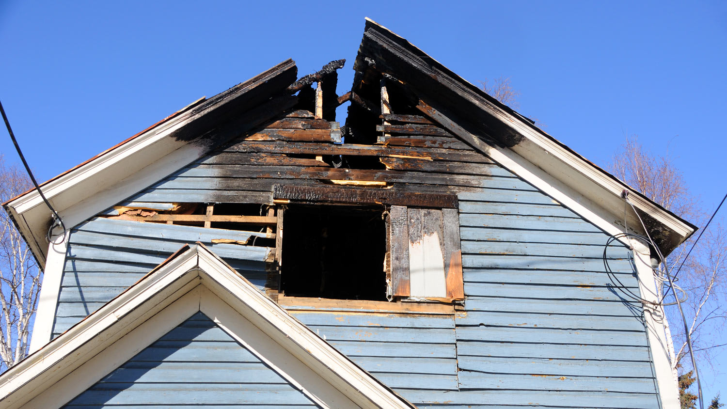 Blue wooden home with the roof burned away