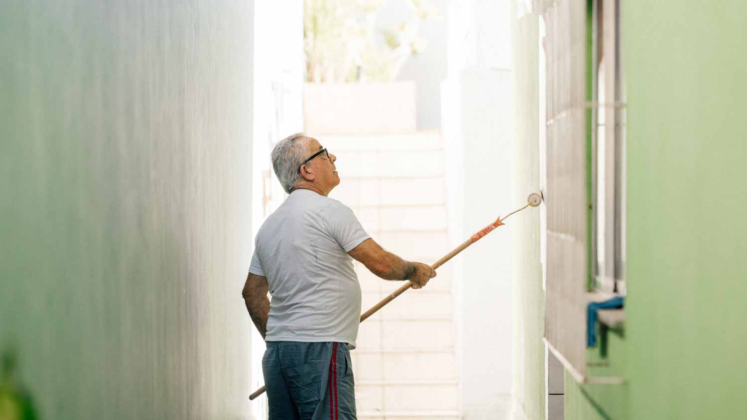 A person uses a long roller brush to paint a green wall.