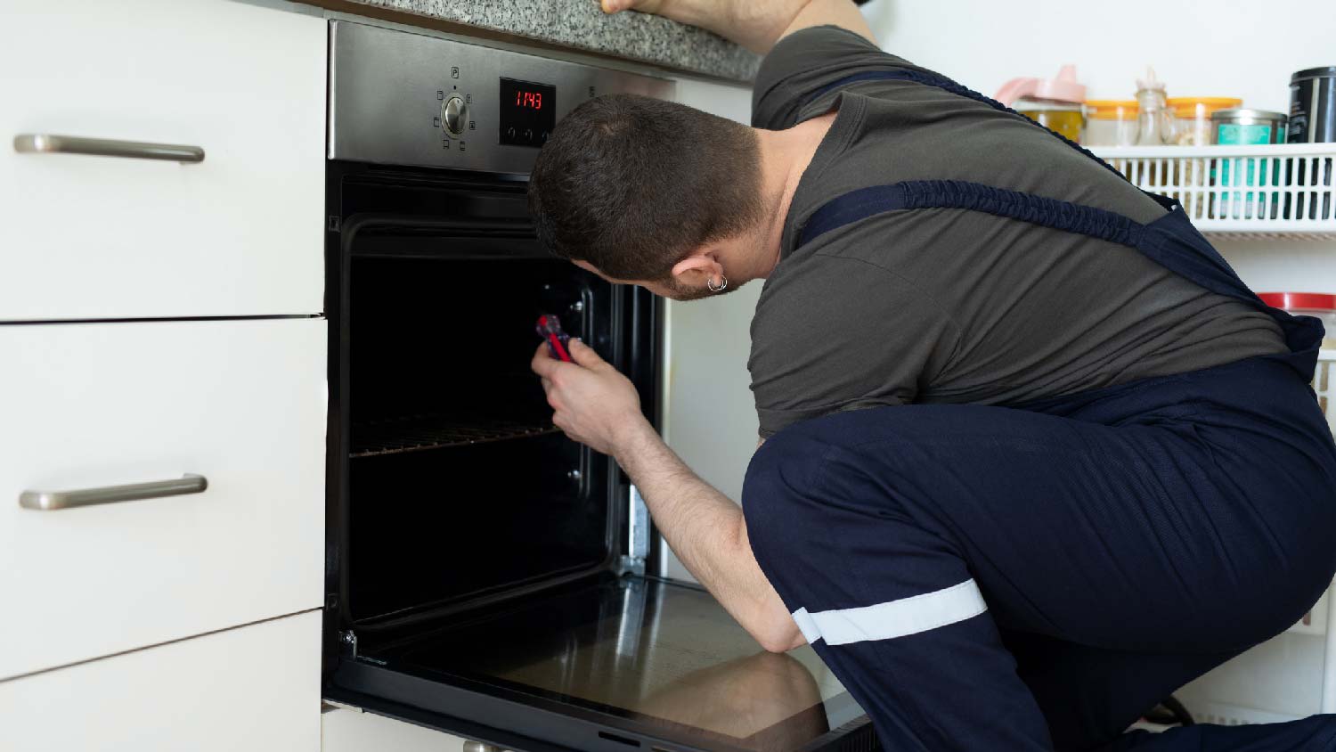 A professional repairing an oven in a kitchen