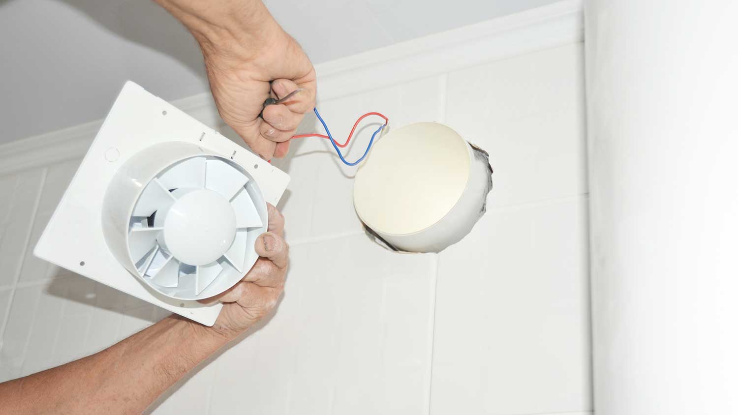 A person installing a bathroom fan