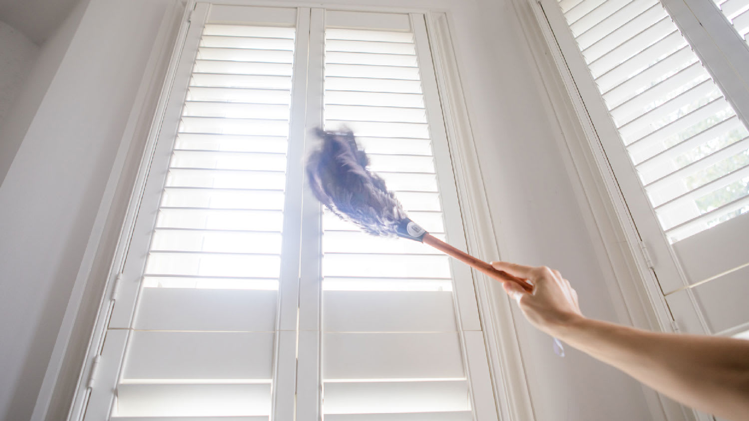 A person using a feather duster to clean shutters