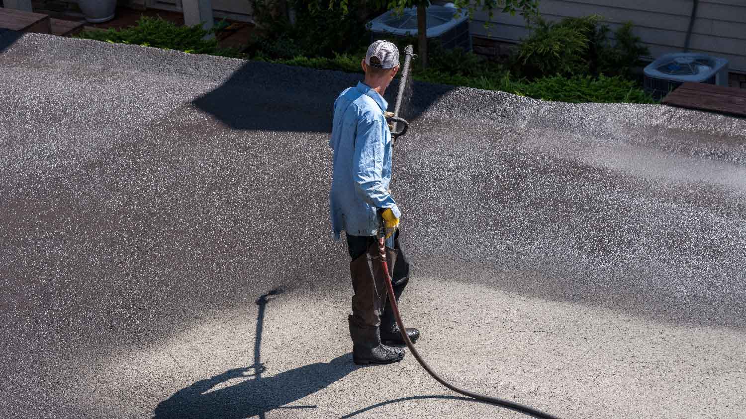 A man spraying sealer to an asphalt driveway