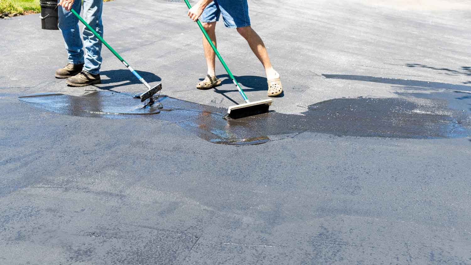Two men applying sealer to an asphalt driveway