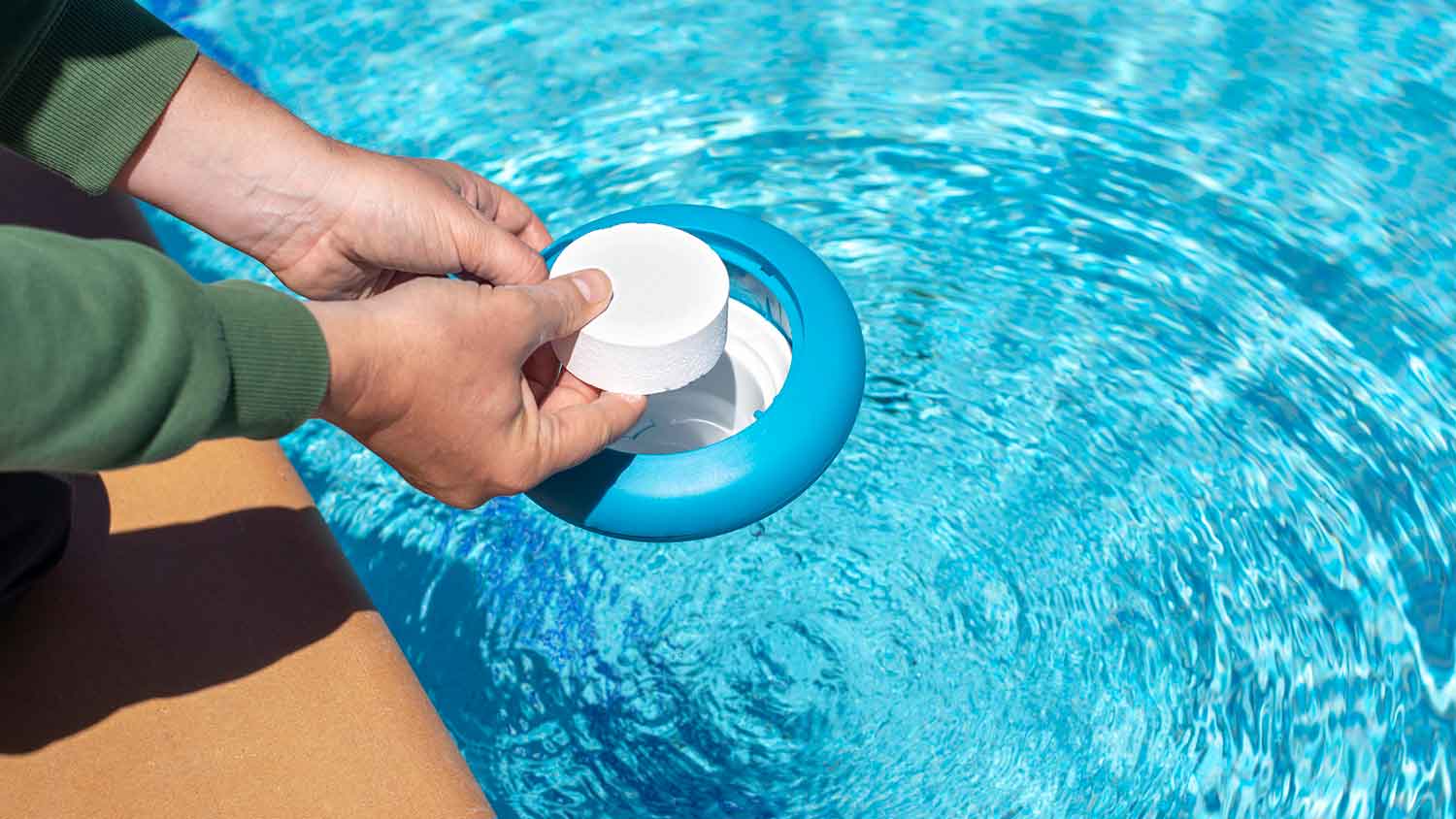 Person adding a pool chlorine tablet into a floating dispenser