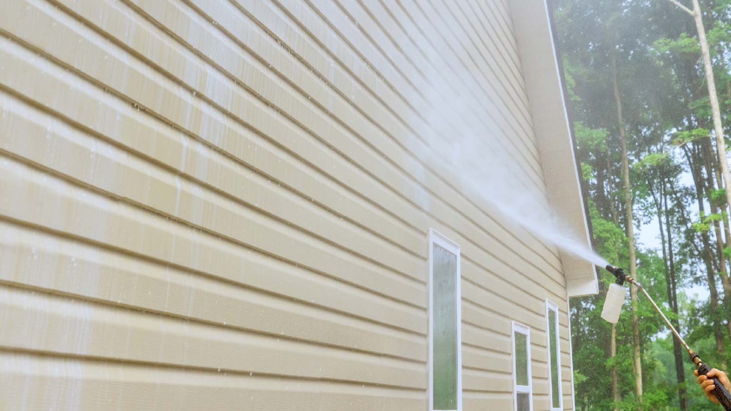 Close-up of a person power washing a house’s siding