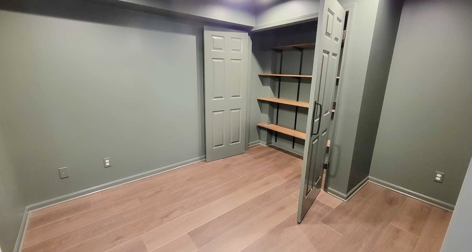 A dark sage green office with a double door closet that has a wooden shelf storage system.