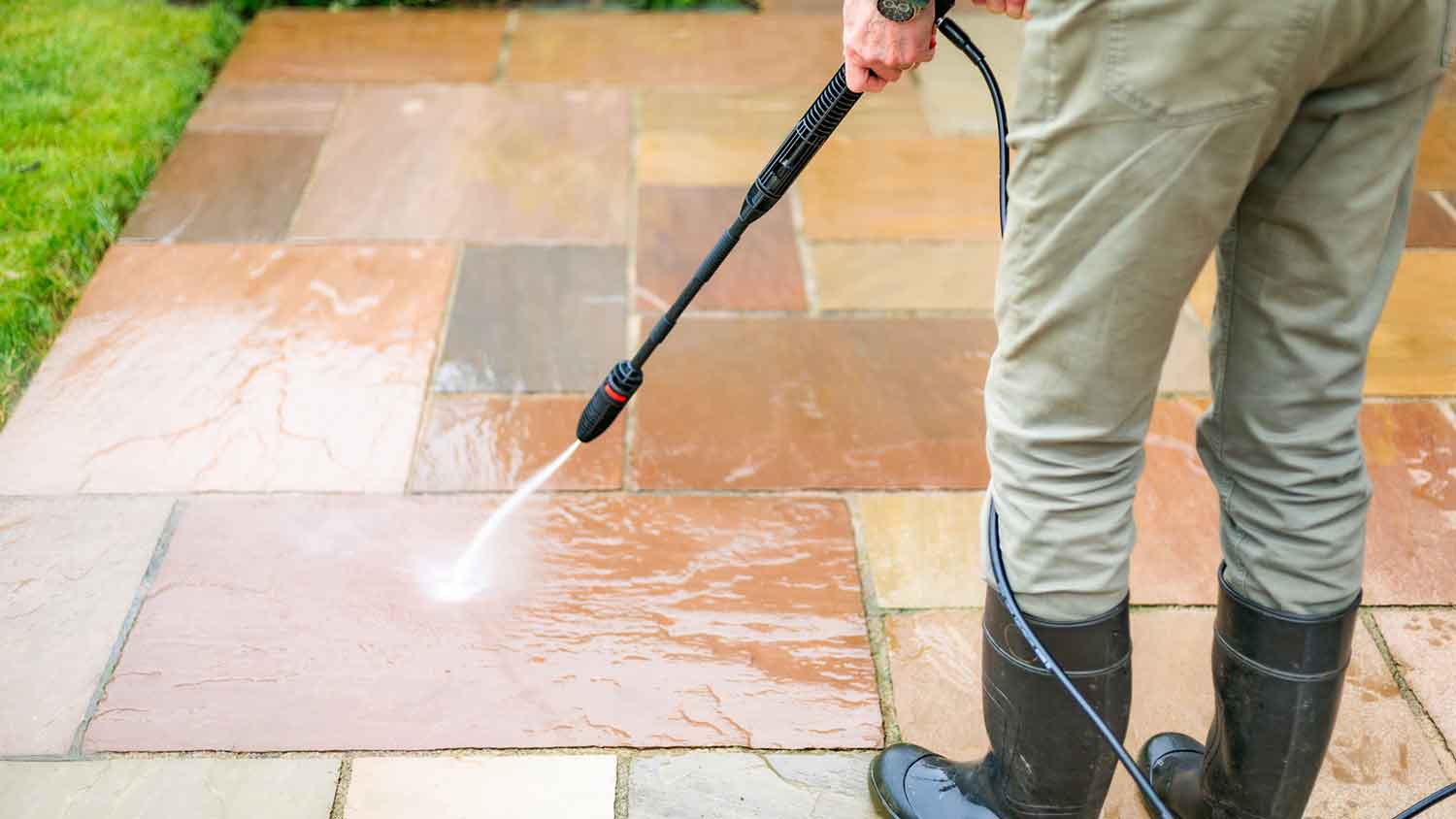 Man using a pressure washer to clean a paver patio