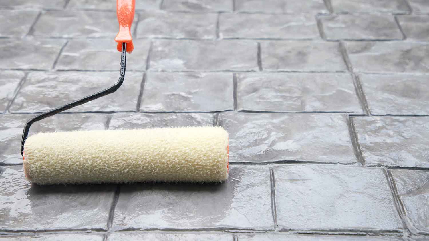 Using a roller to apply sealer on patio pavers
