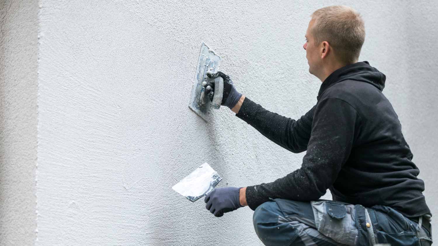 A man applying stucco to a house
