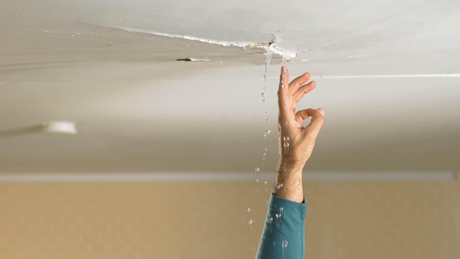 man reaching up to touch water falling from crack in ceiling