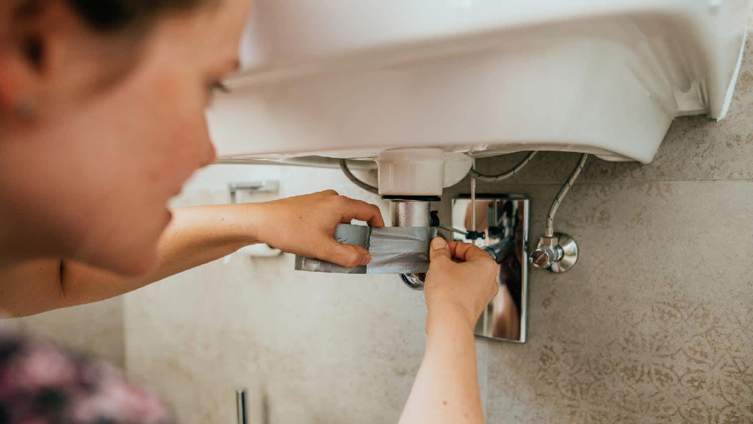 A woman stoping a leak from plumbing pipes