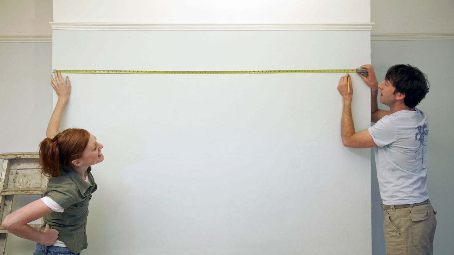 couple measuring wall in empty apartment