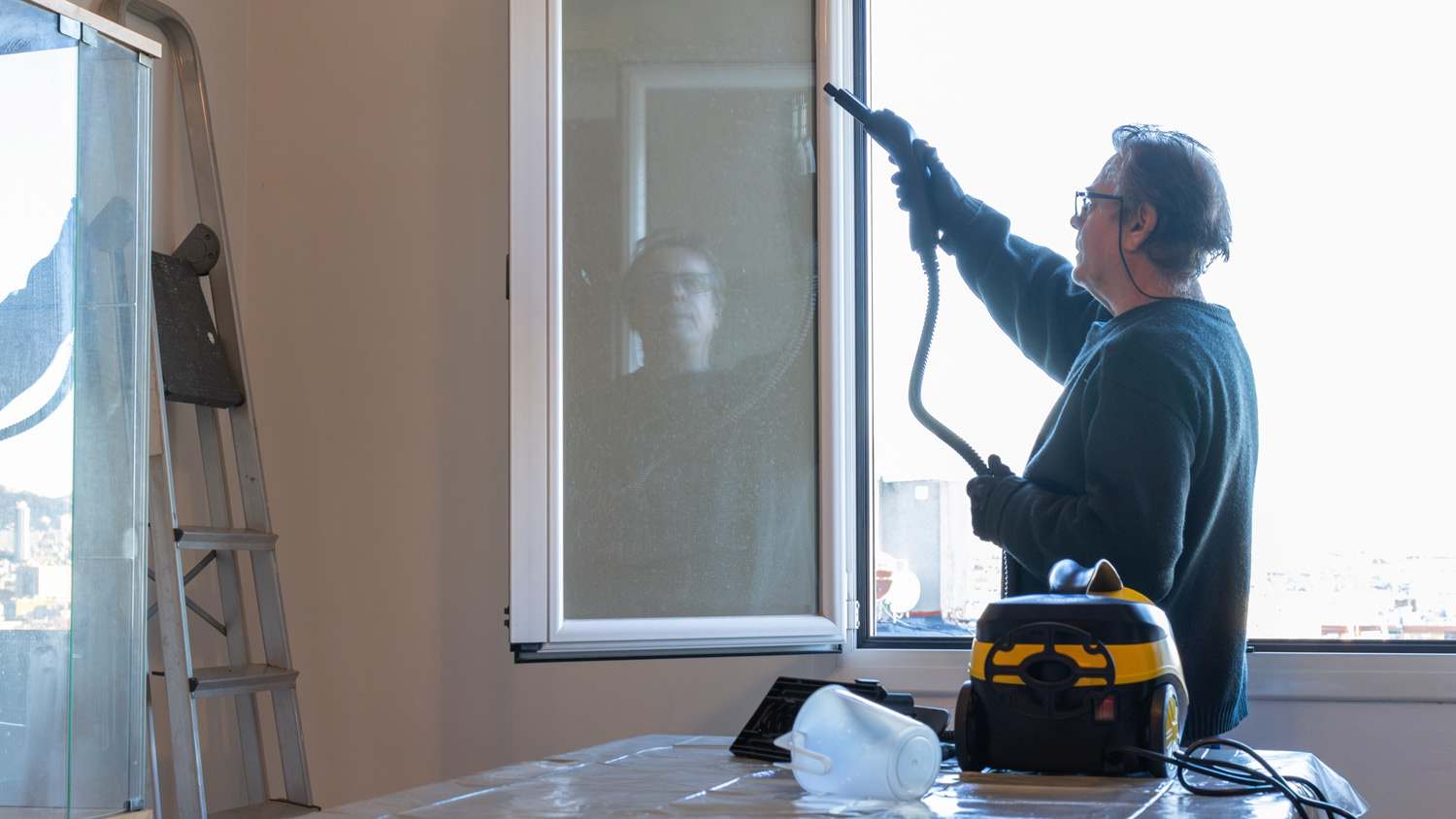 man doing housework at home using a steam cleaning appliance for hygiene to clean the windows