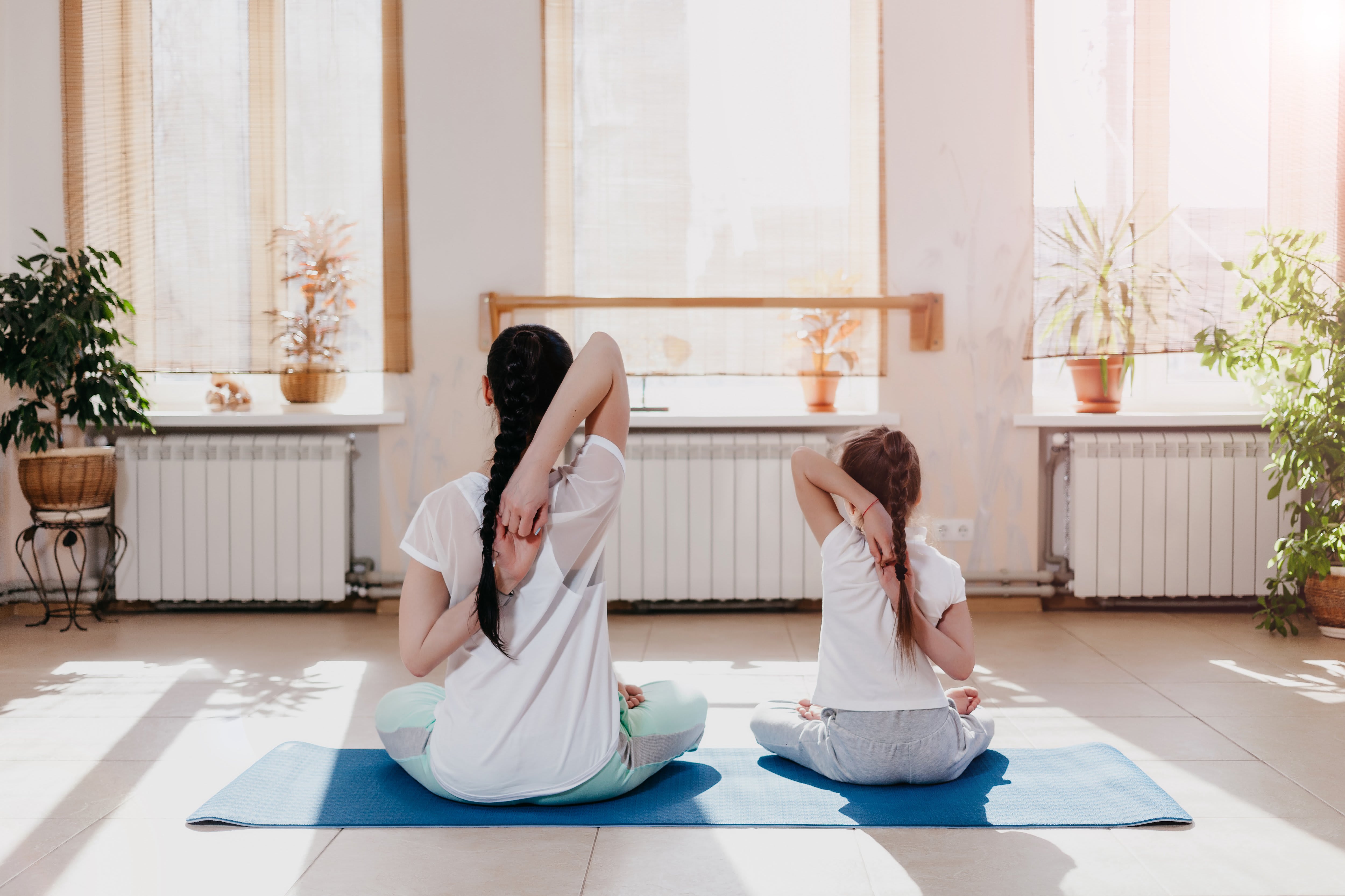 A mom and daughter do yoga together in their home gym while looking out the window