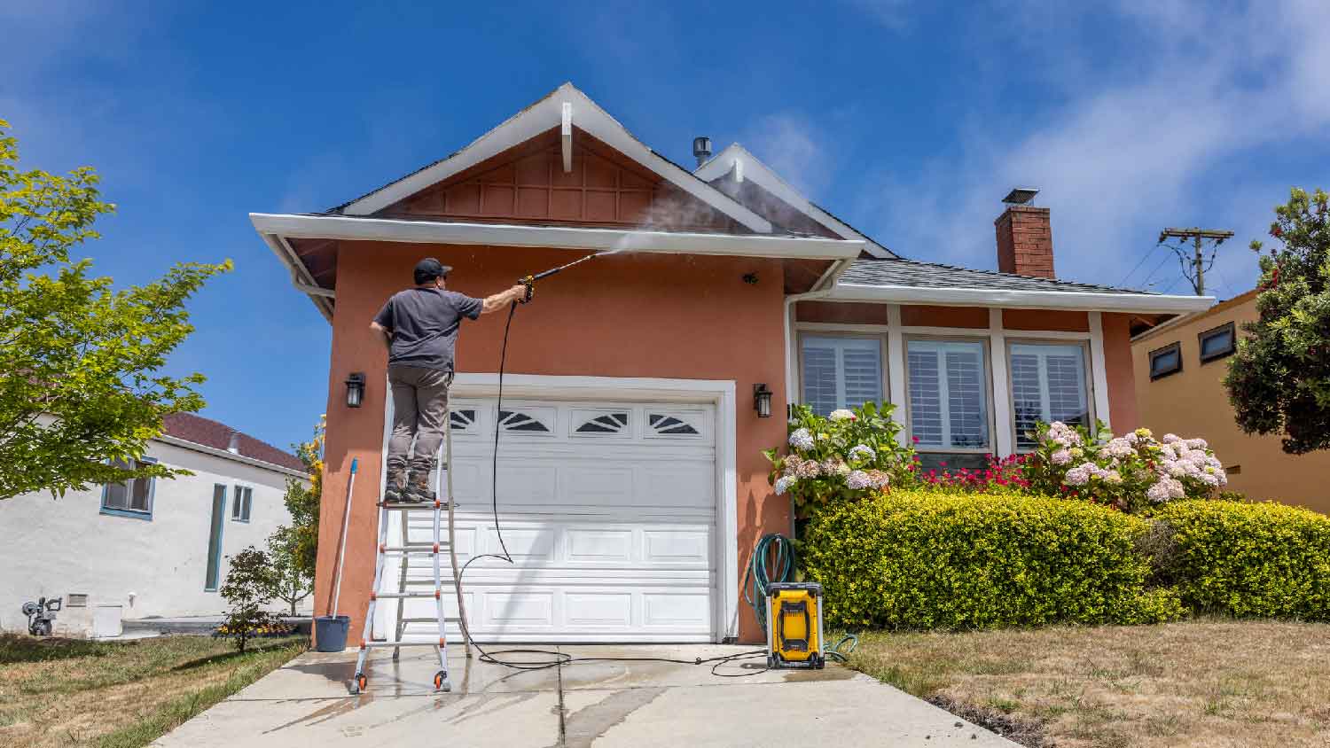 A man on a ladder power washing the exterior of a house