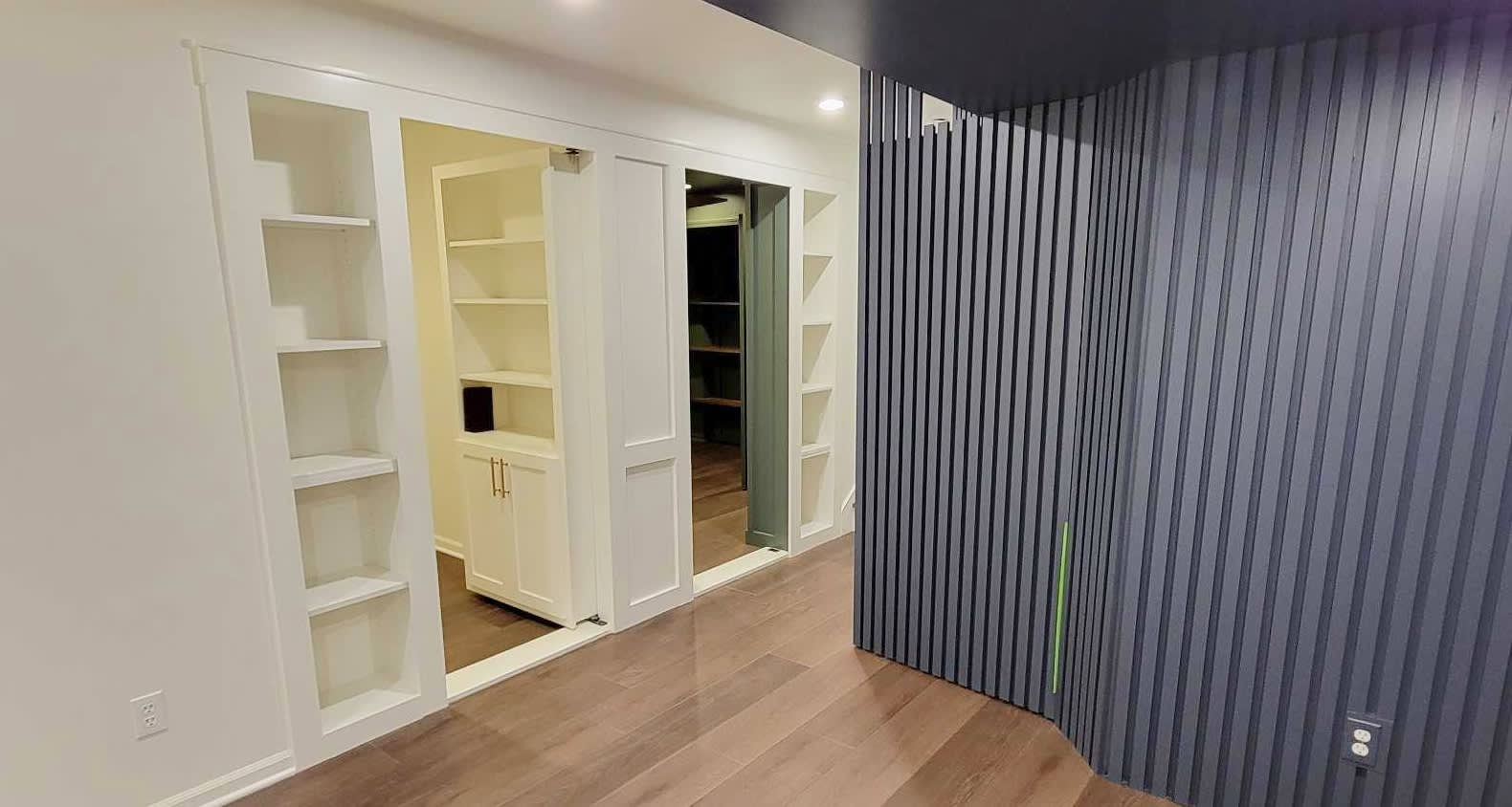 Two Murphy doors disguised as bookshelves open into an office and a bathroom. There is a navy blue slat accent wall on the right.